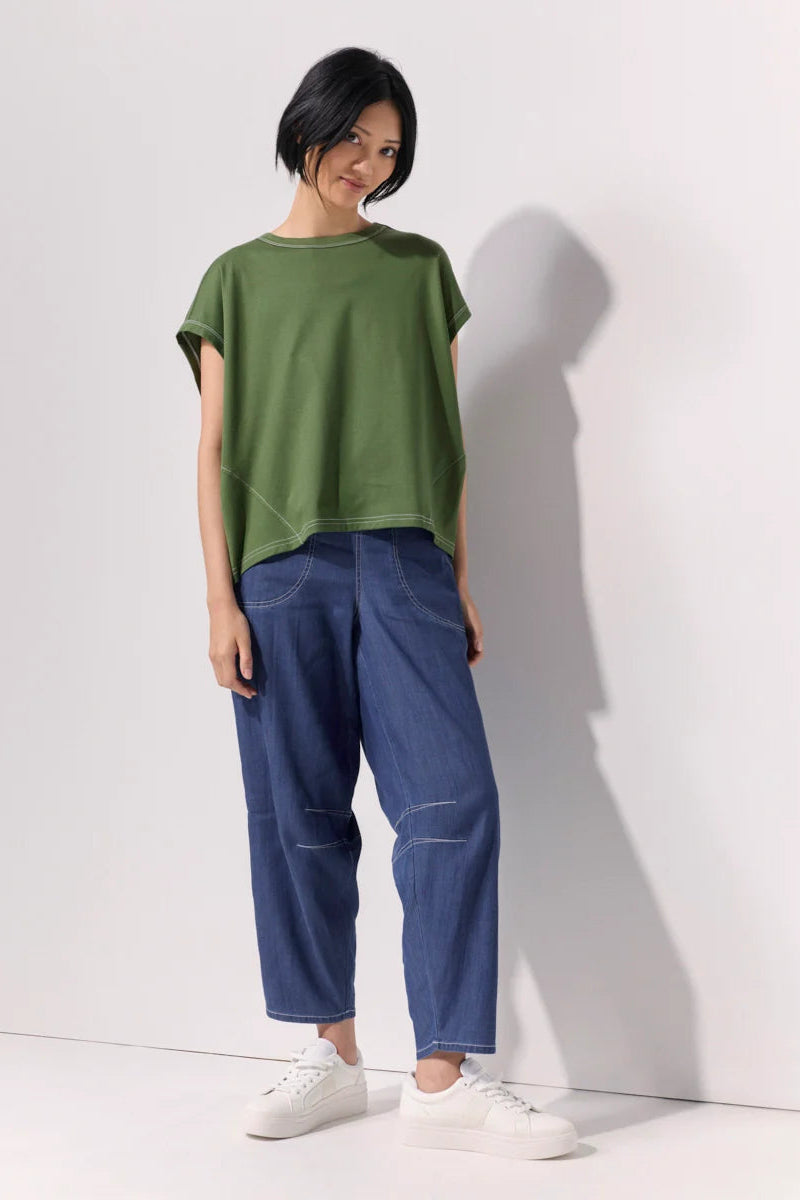 Woman wearing a green tee shirt and wide leg 7/8 light denim pants with contrast top stitching and pockets against a white background.