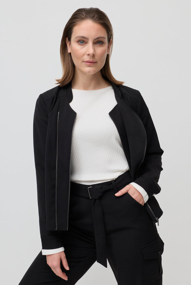 Woman wearing a black jacket over a white shirt and black pants on a light gray background
