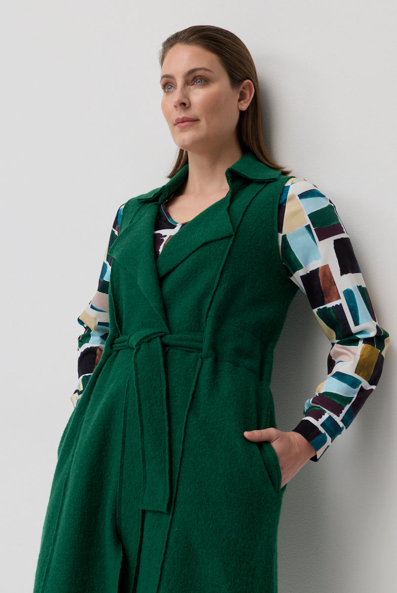 Woman wearing a green coat over a colorful patterned shirt against a plain background