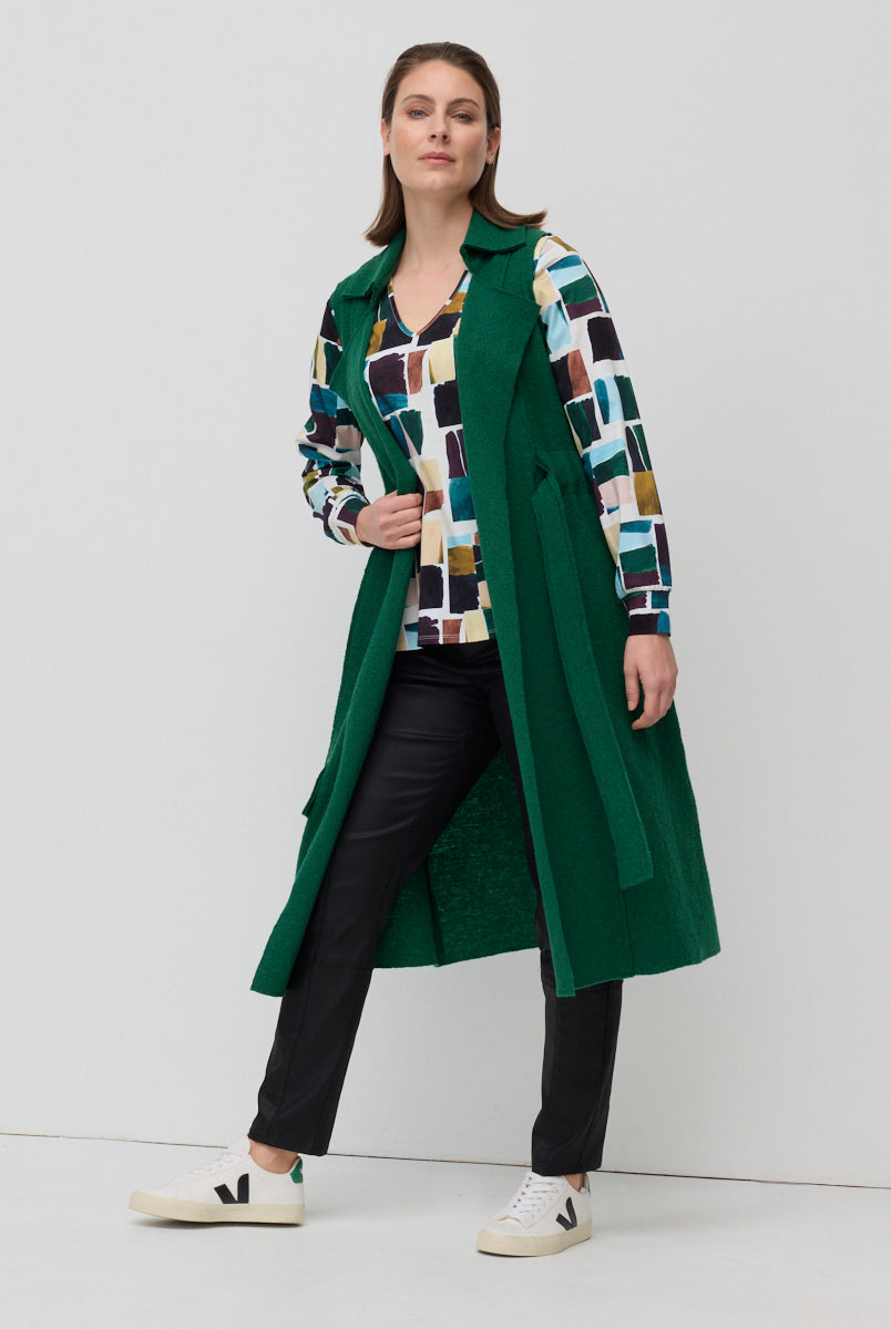 Woman wearing a green coat over a patterned shirt with a white background