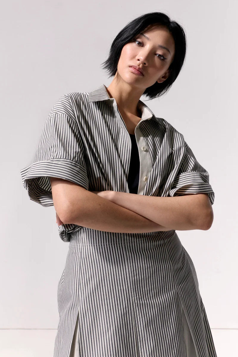 Woman wearing a striped overshirt with collar and cuffed sleeves against a white background.