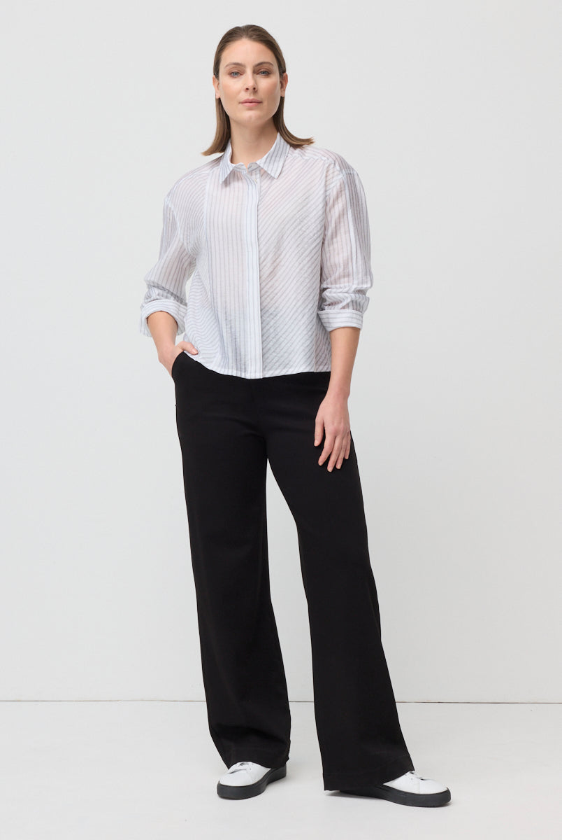 Woman wearing a white blouse with black patterns and black pants on a white background