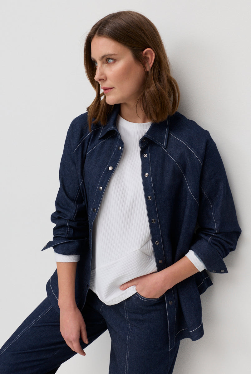 Woman wearing a navy denim jacket over a white shirt against a light gray background