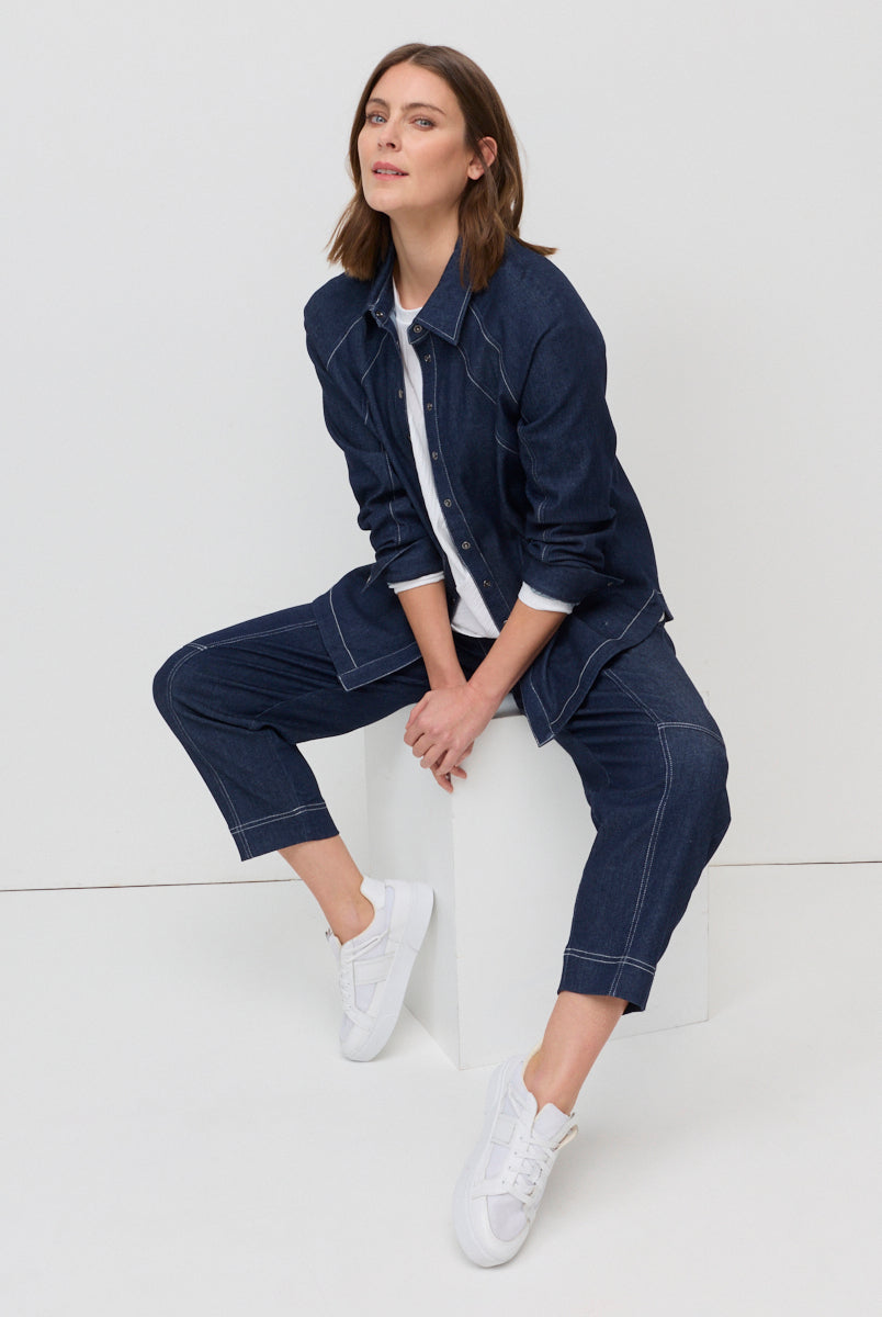 Woman wearing a navy denim outfit sitting on a white surface