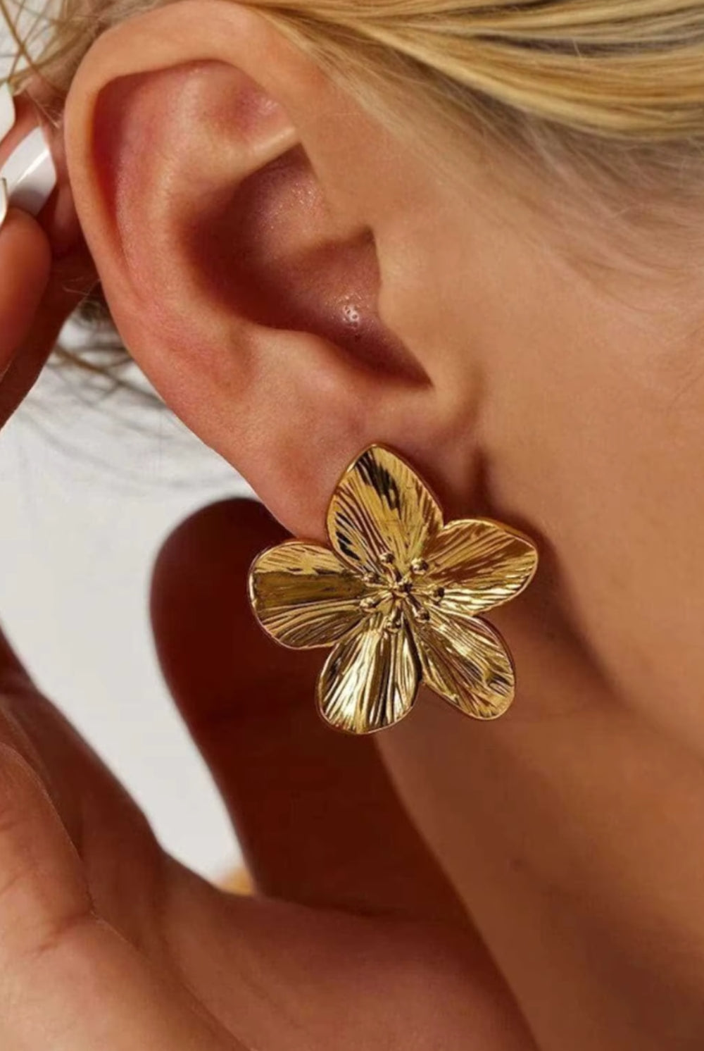 Gold floral earring worn by a person with a blurred background