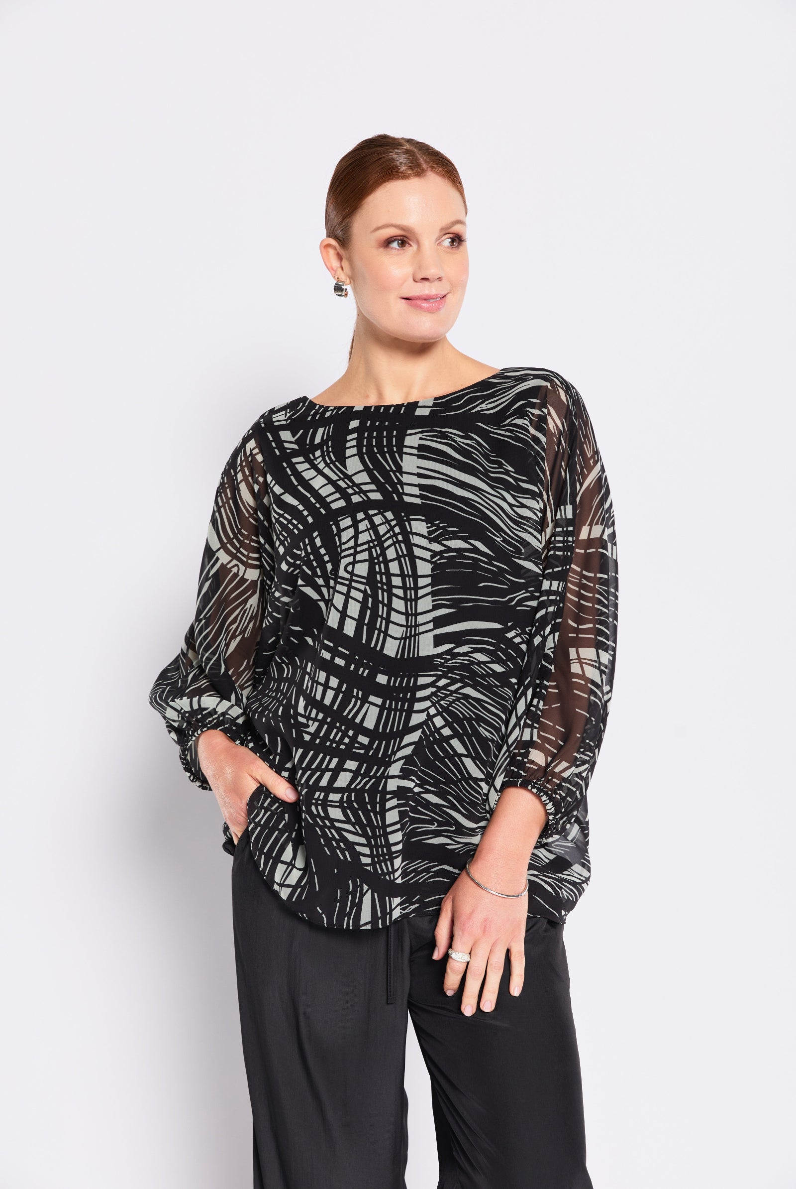 Woman wearing a black and sage patterned top on a white background