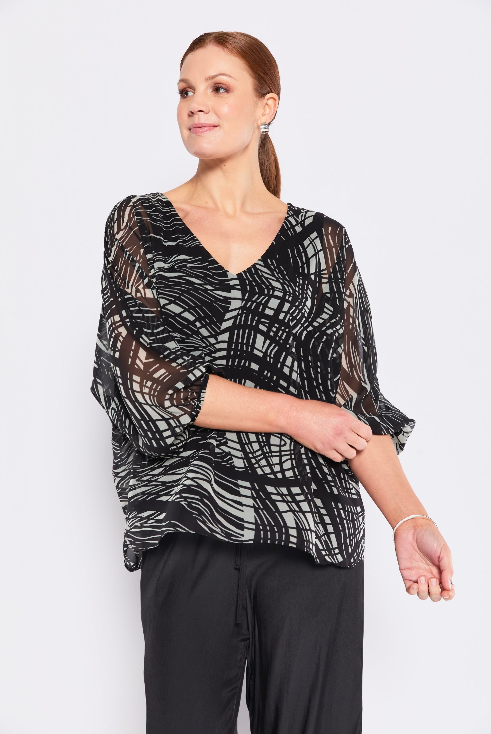 Woman wearing a black and sage patterned top with black pants on a white background