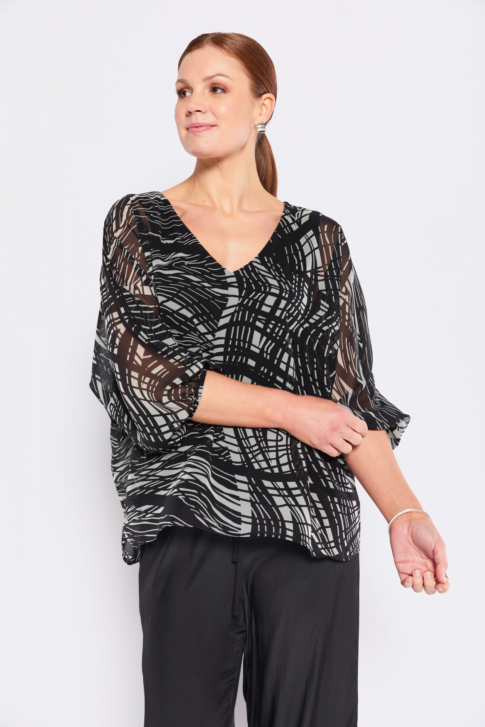 Woman wearing a black and sage patterned top with black pants on a white background