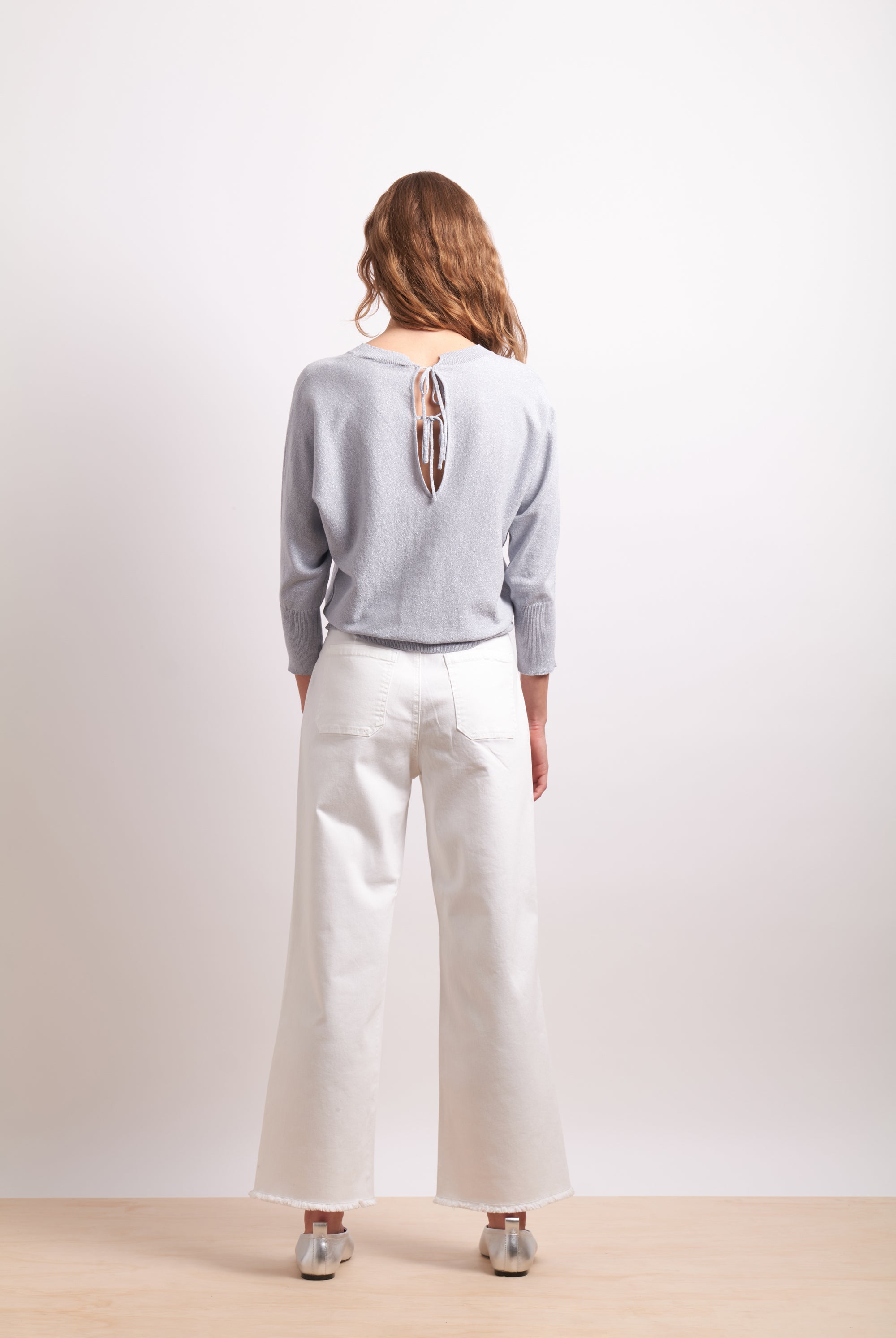 Person wearing a light gray sweater and white pants on a plain background