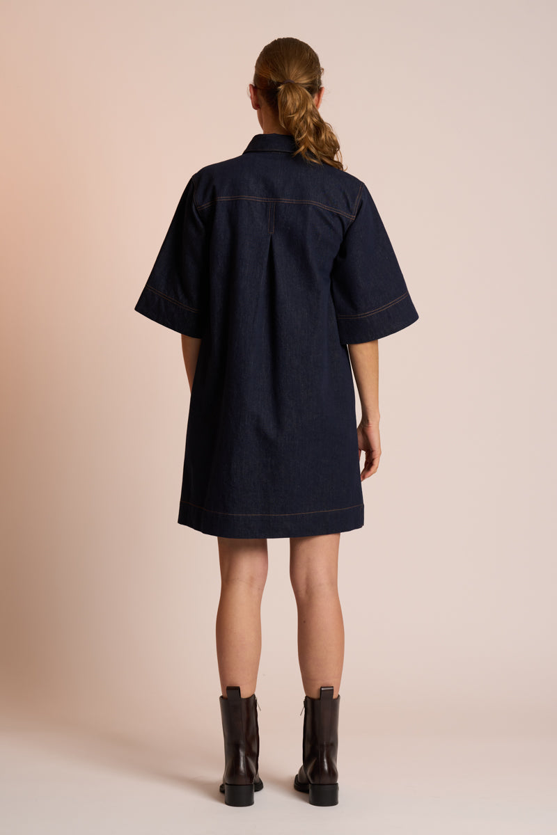 Person wearing a navy dress with short sleeves on a beige background back angle