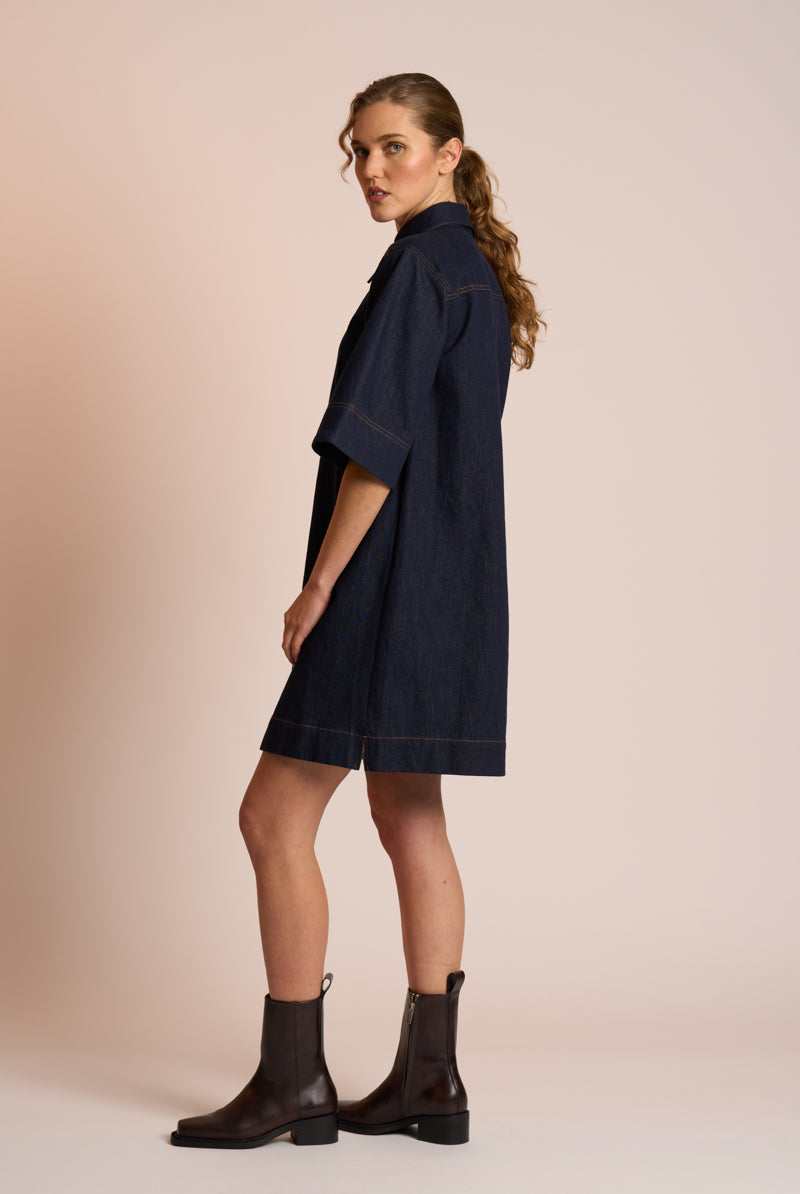 Woman wearing a navy dress and black boots against a beige background side angle
