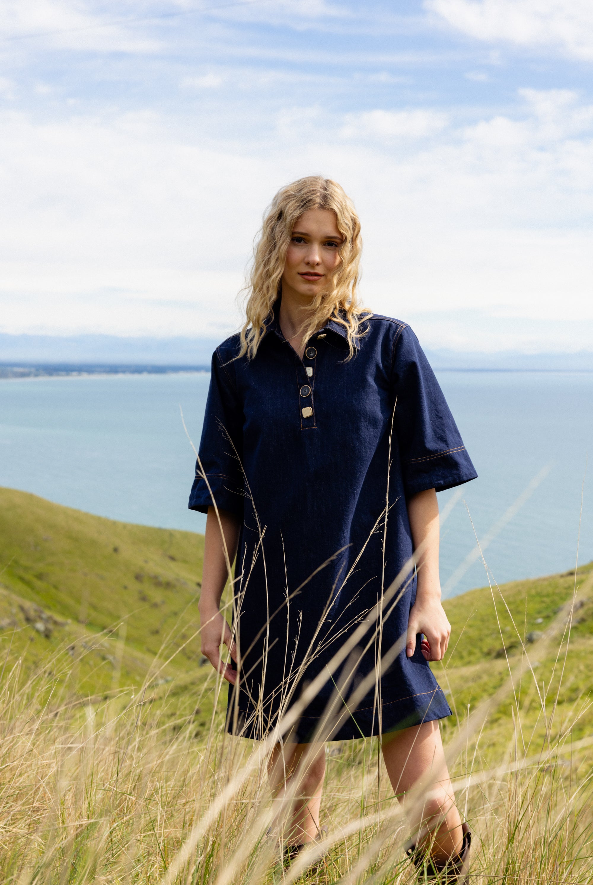 Woman in a navy dress standing in tall grass with a scenic background
