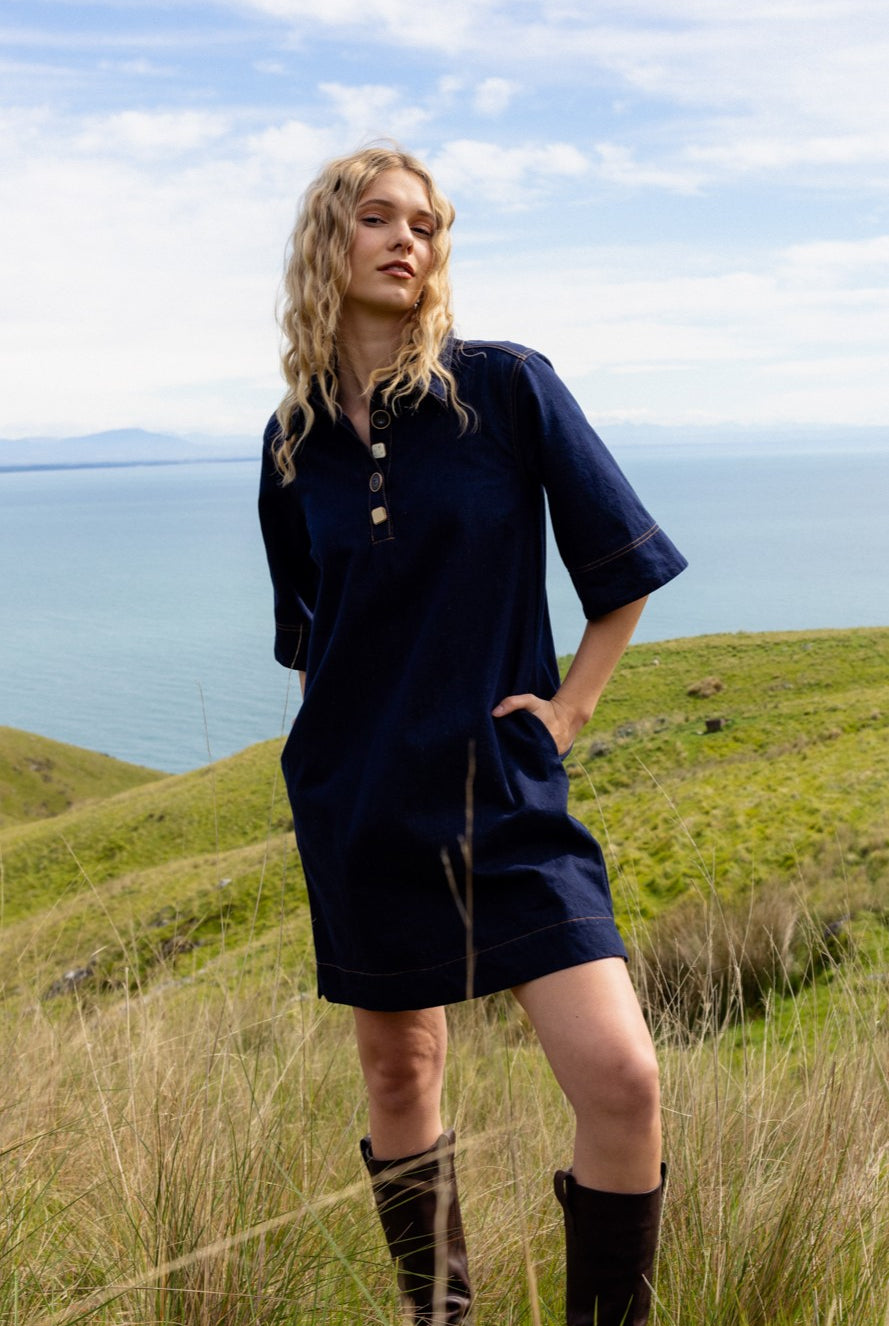 Woman in a navy dress standing on a grassy hill with ocean view