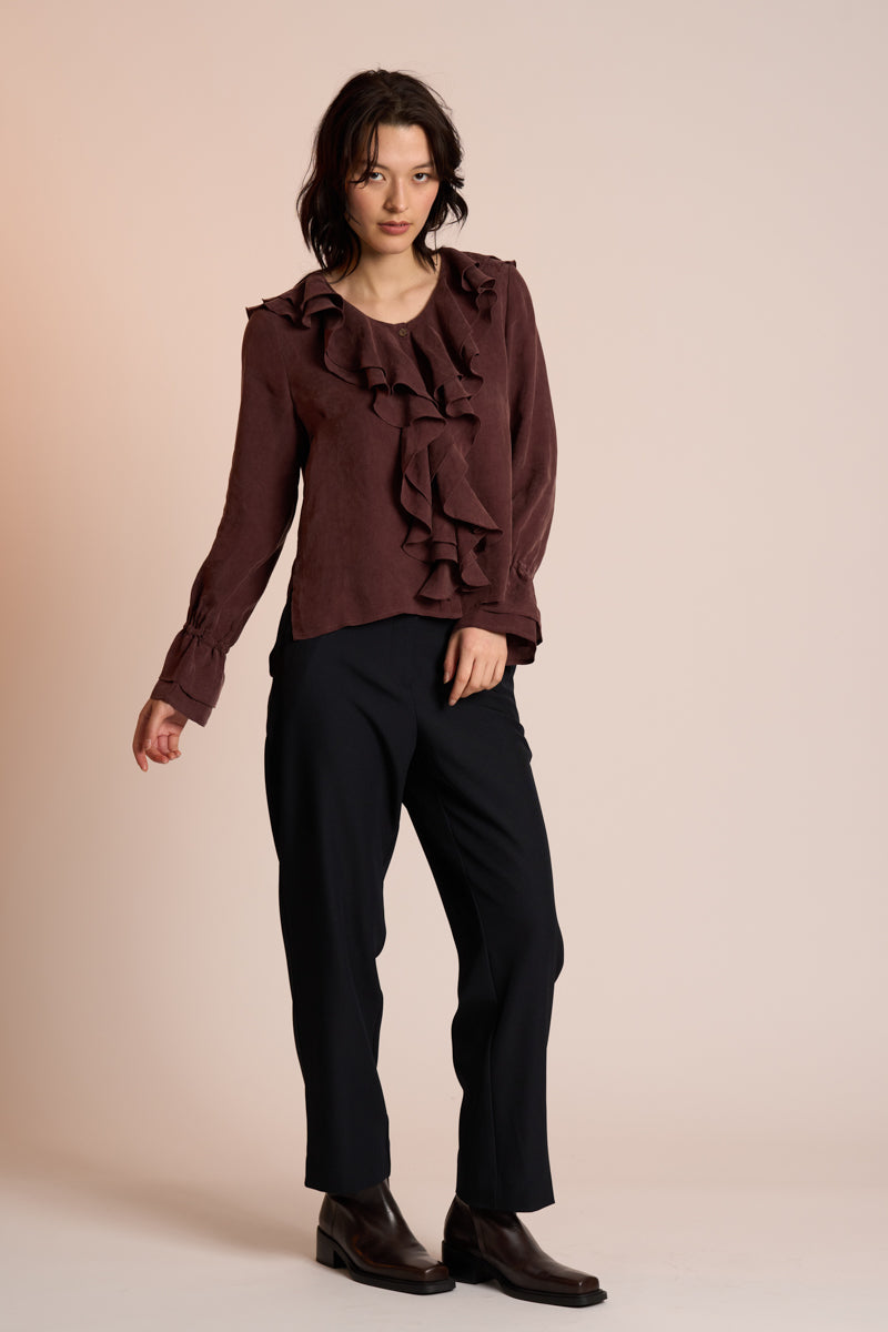 Woman wearing a brown ruffled blouse and black pants on a beige background
