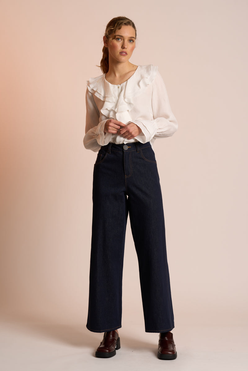 Woman wearing a white blouse and dark pants against a beige background