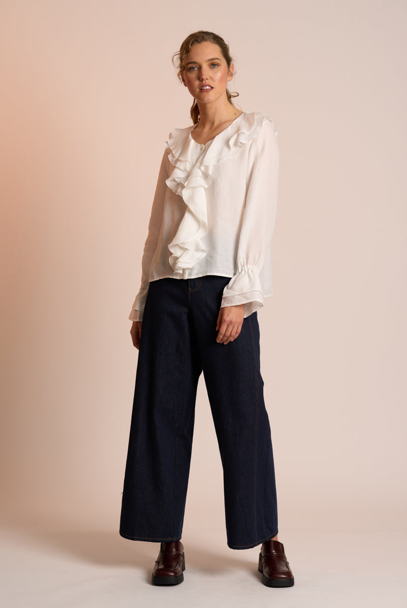 Woman wearing a white blouse with ruffles and dark pants on a beige background