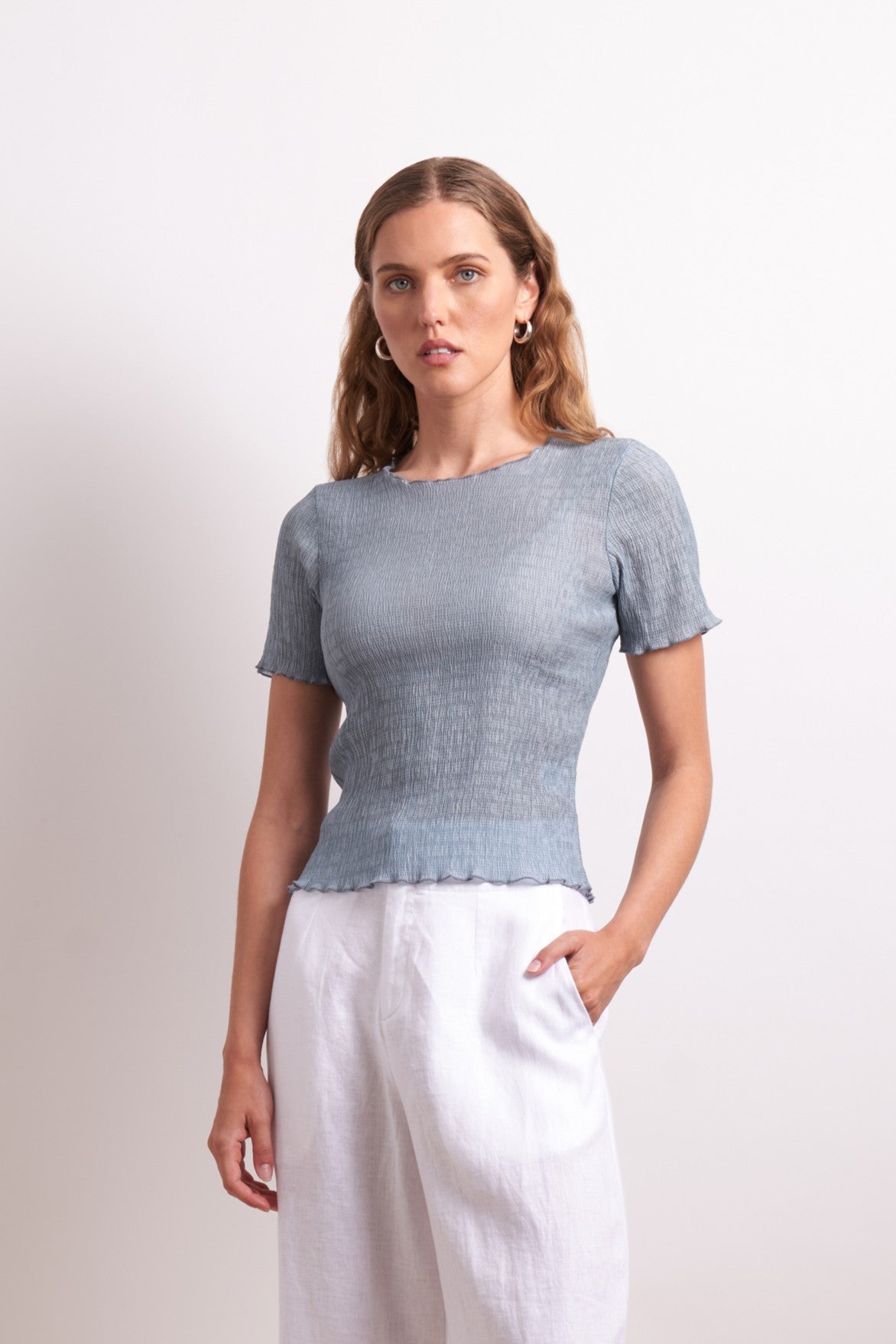 Woman wearing a light blue top and white pants against a plain background