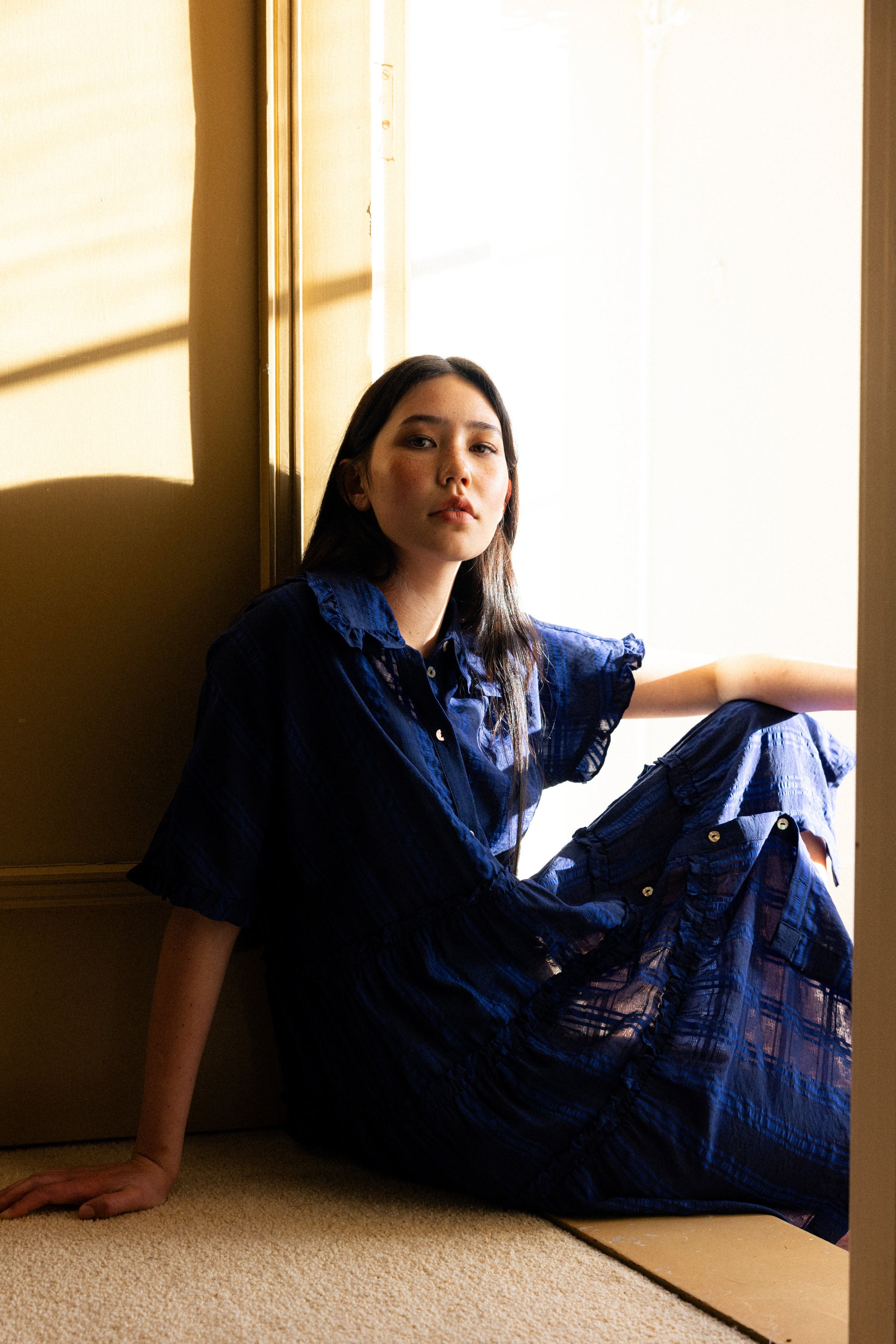 Woman in a blue dress sitting by a window with sunlight streaming in
