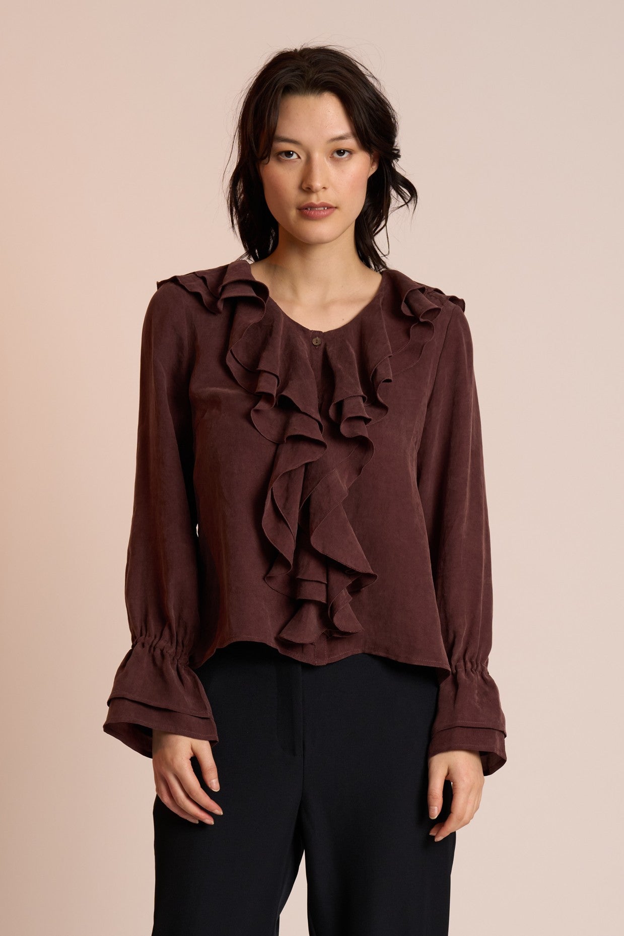 Woman wearing a brown ruffled blouse against a beige background
