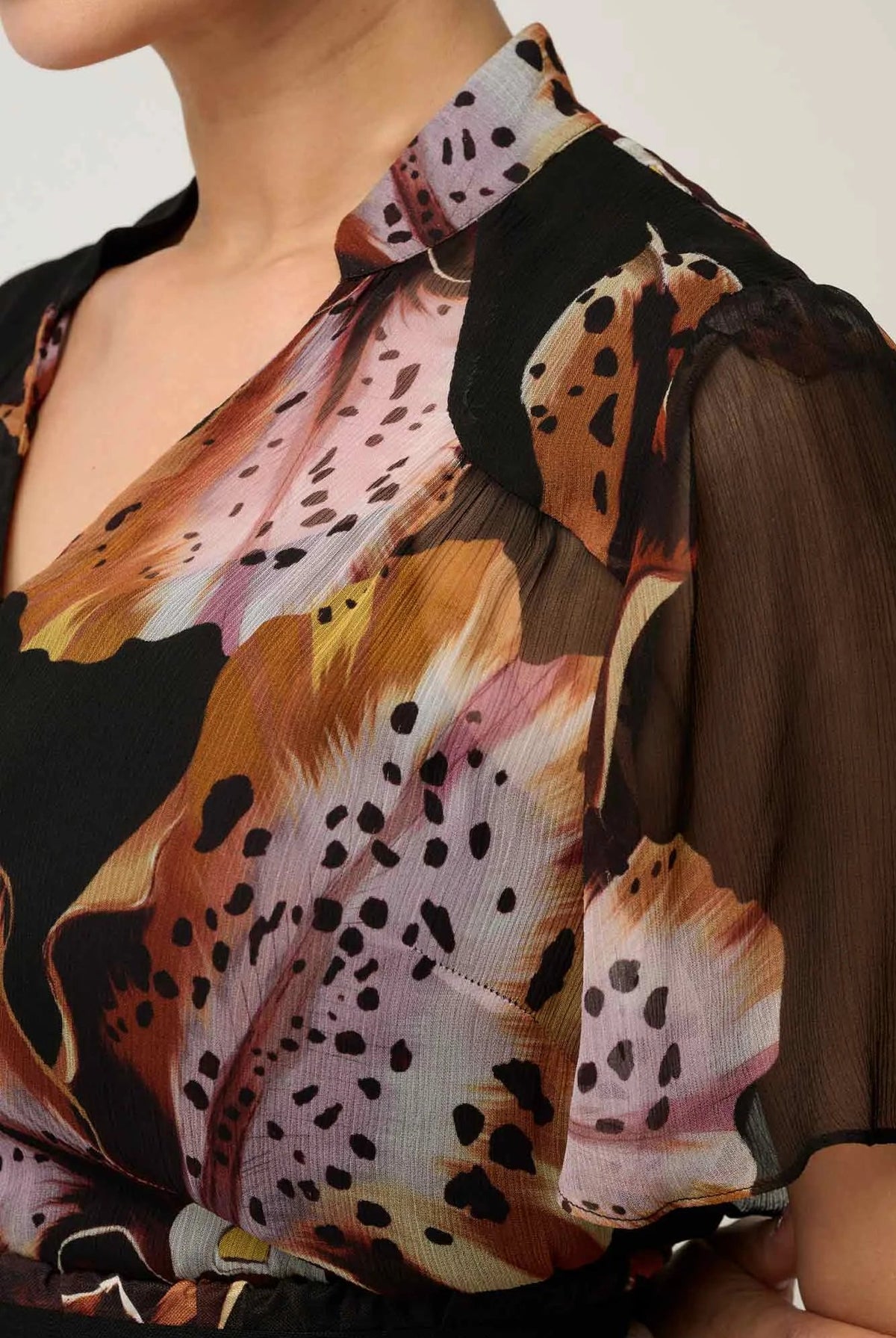 Woman wearing a black floral floaty chiffon dress with tie waist and short sleeves against a white background
