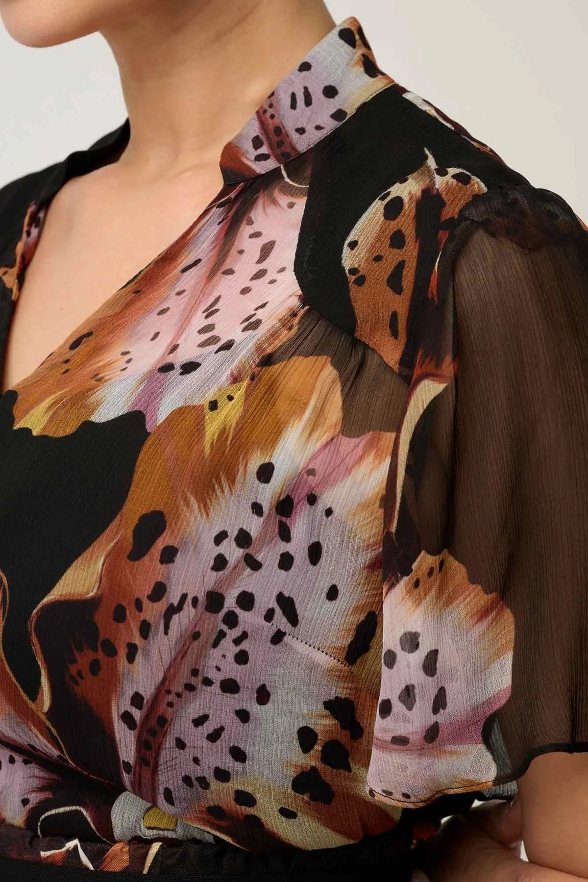 Woman wearing a black floral floaty chiffon dress with tie waist and short sleeves against a white background