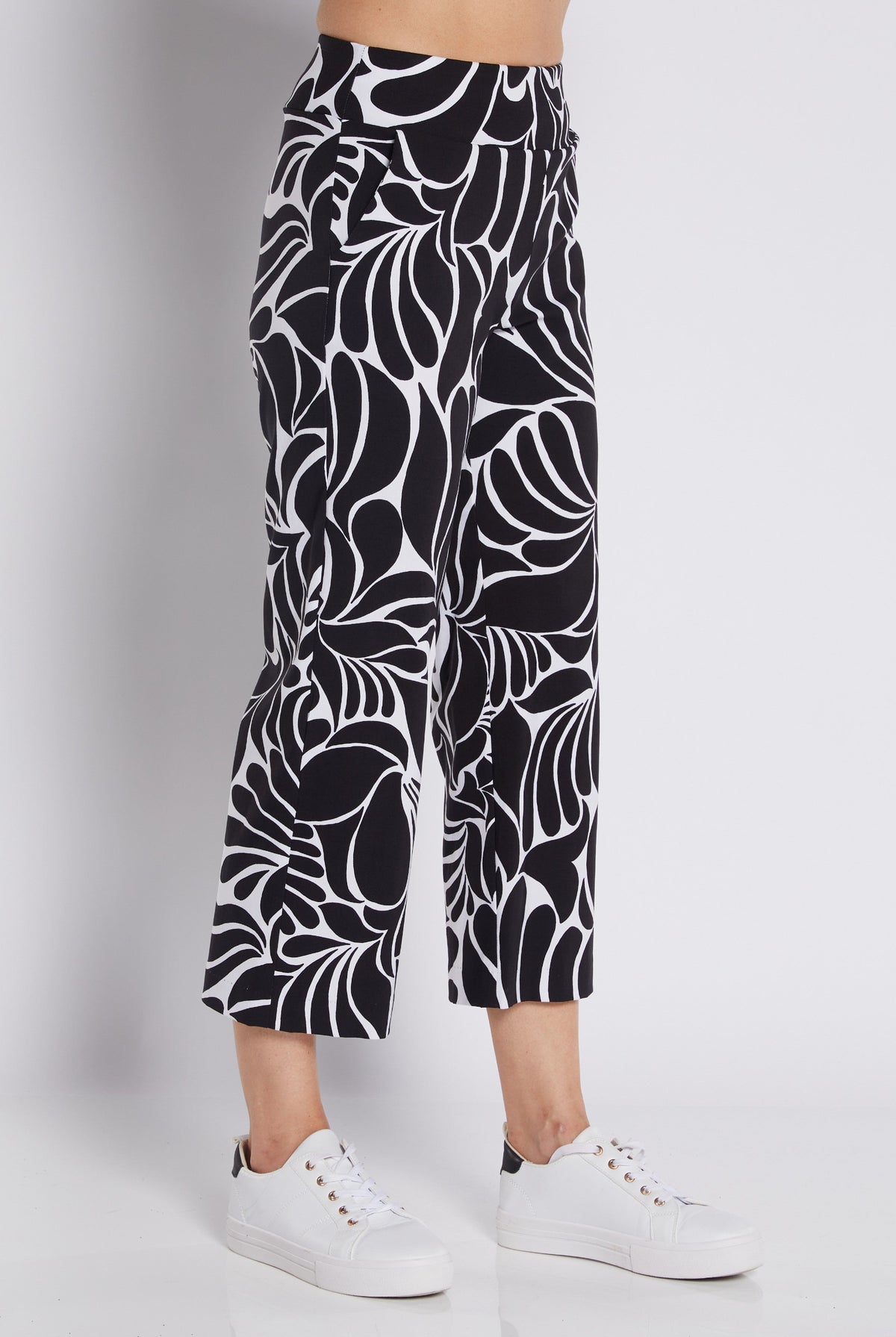 Black and white abstract patterned cropped pants worn by a model with white sneakers, photographed against a light gray studio background.