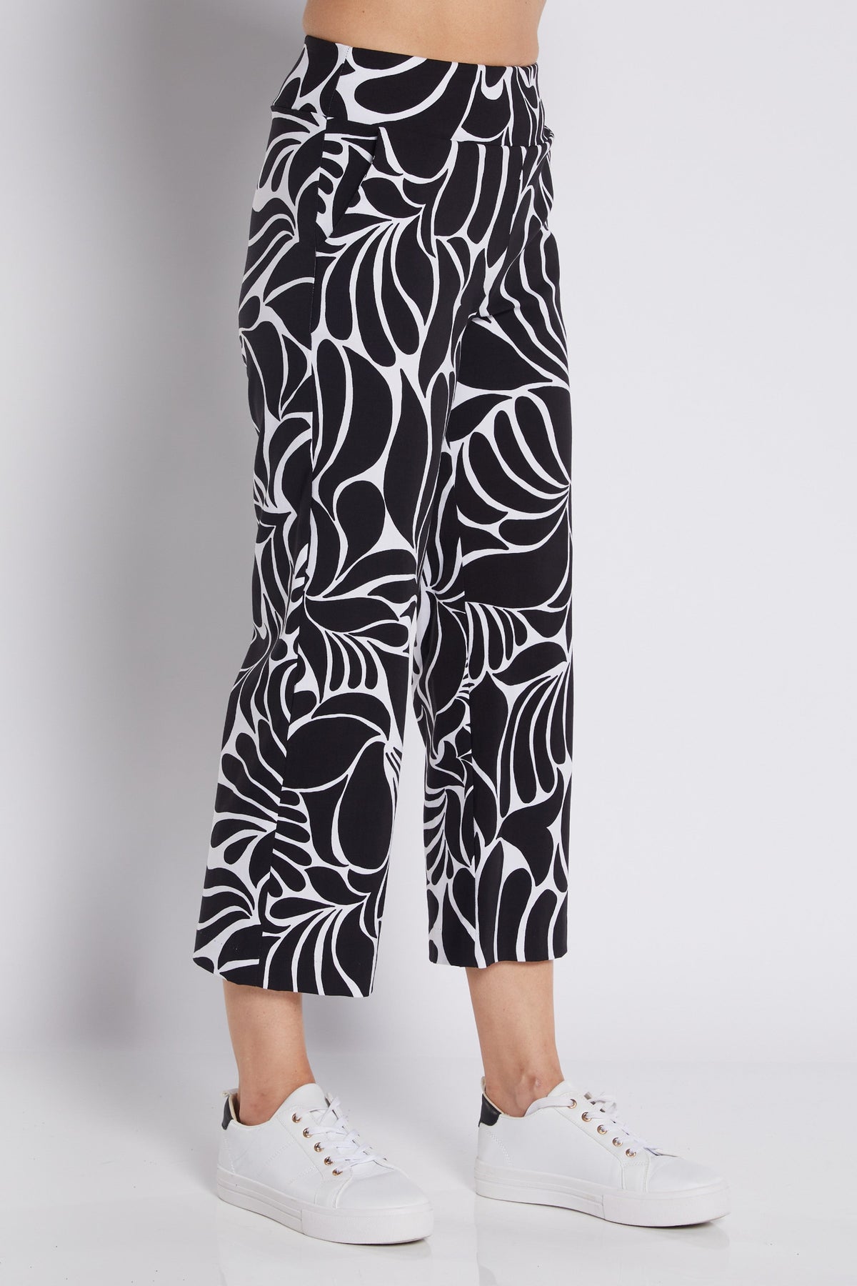 Black and white abstract patterned cropped pants worn by a model with white sneakers, photographed against a light gray studio background.