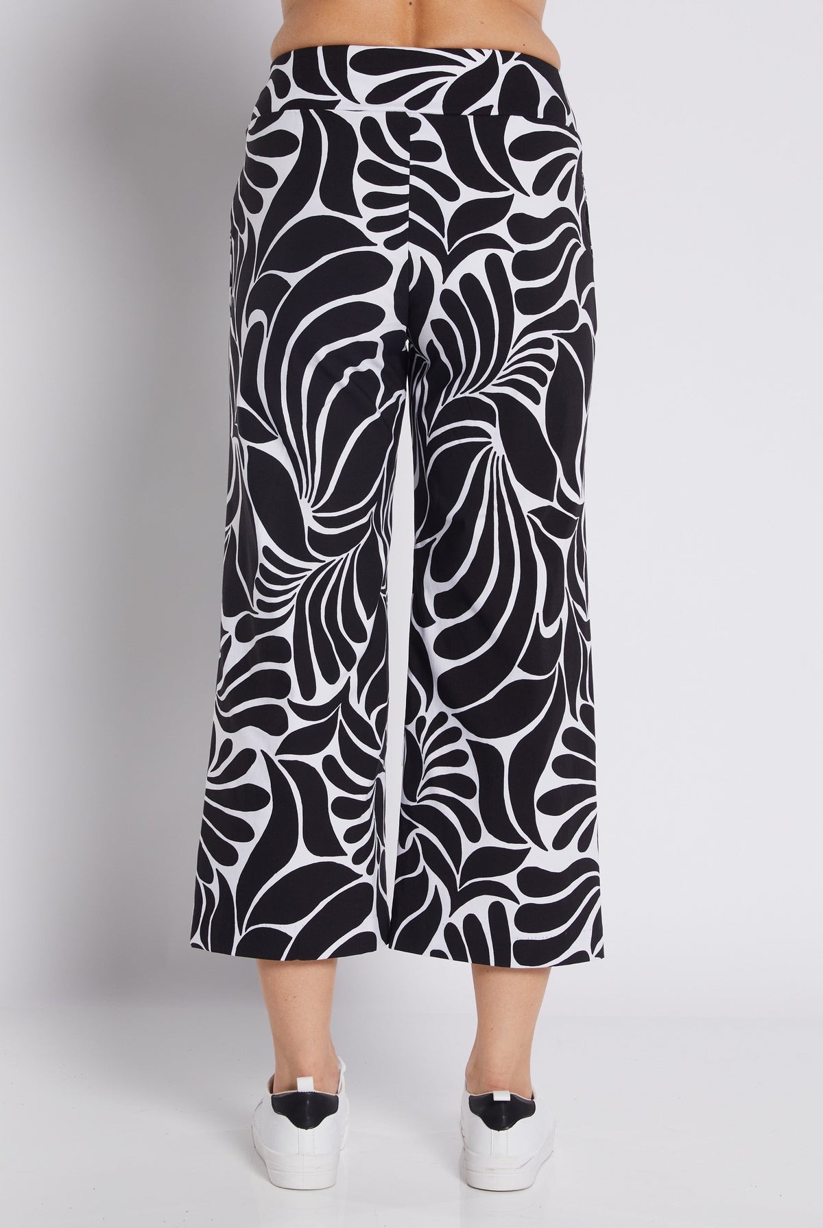 Black and white abstract patterned cropped pants shown on a model from the back, paired with white platform sneakers against a light gray studio background.