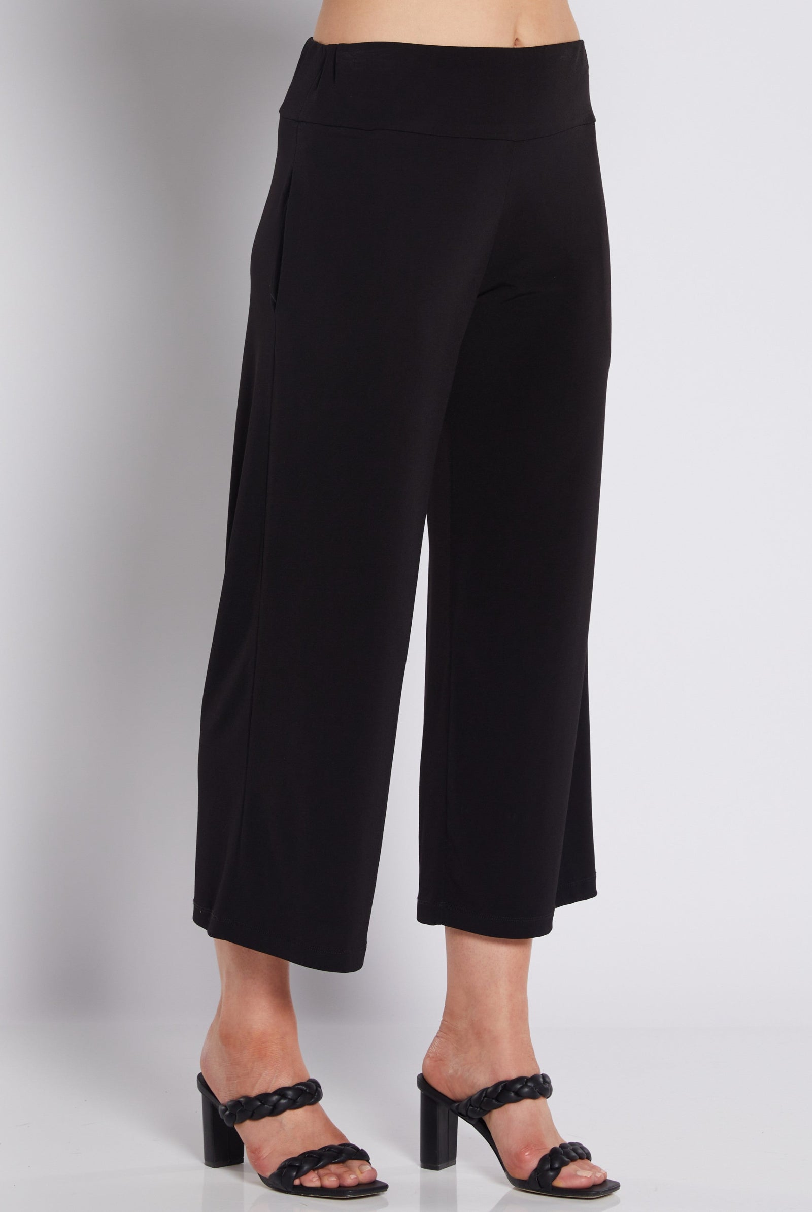 Black cropped wide-leg pants shown on a model from the waist down, paired with black heeled sandals against a light gray studio background.