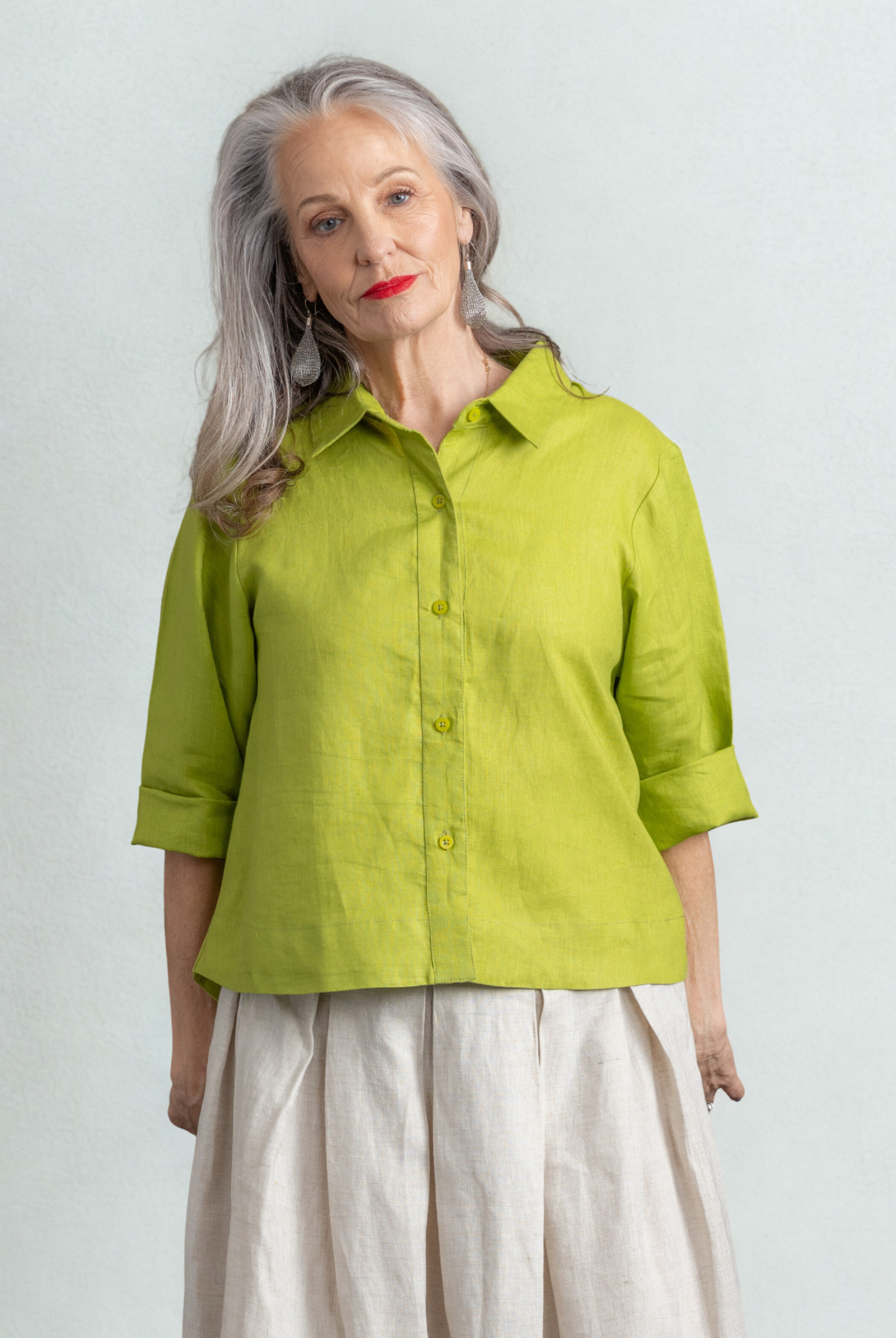 Woman wearing a green shirt and white pants against a light gray background