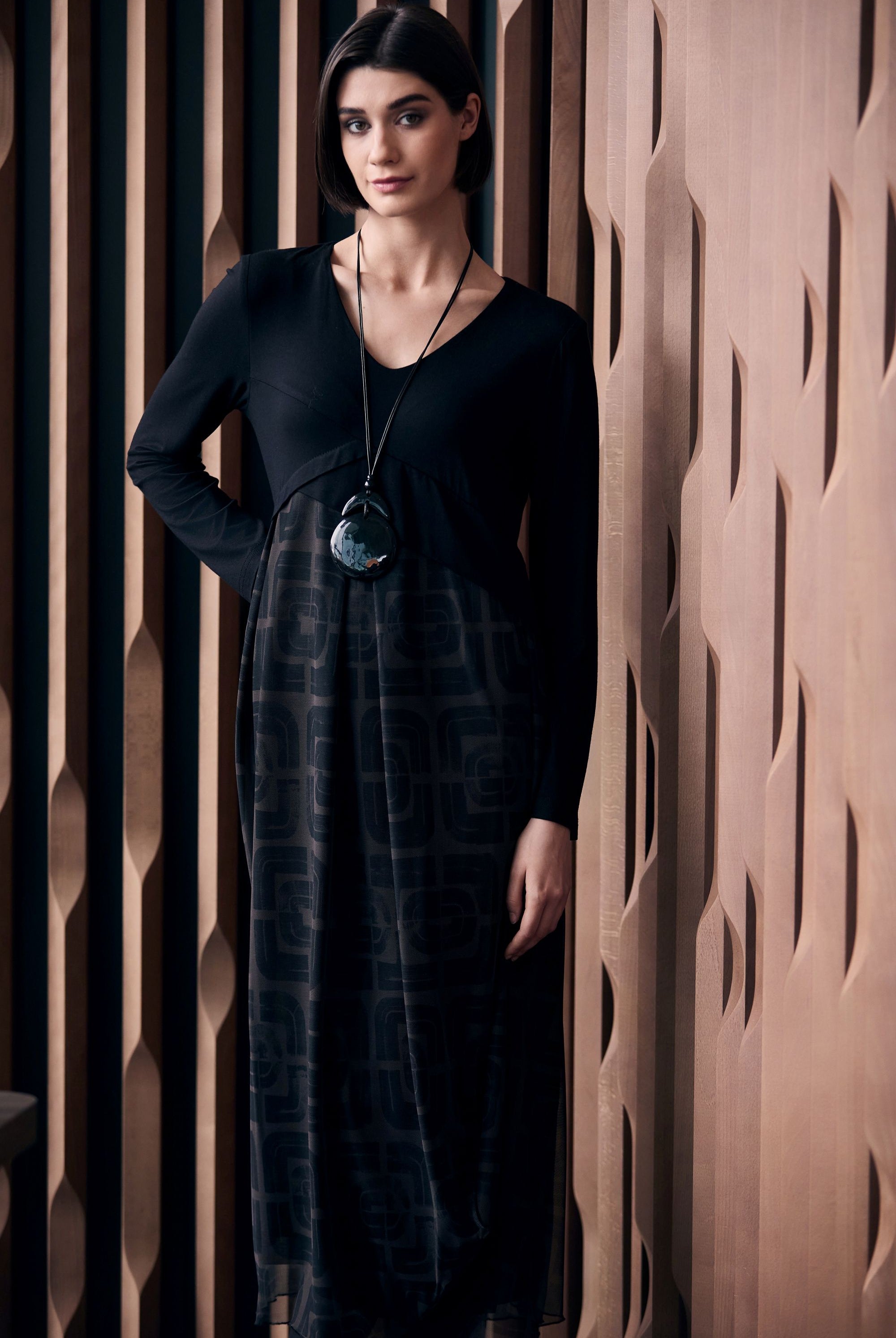 Woman wearing a black and brown patterned dress standing against a textured wall.