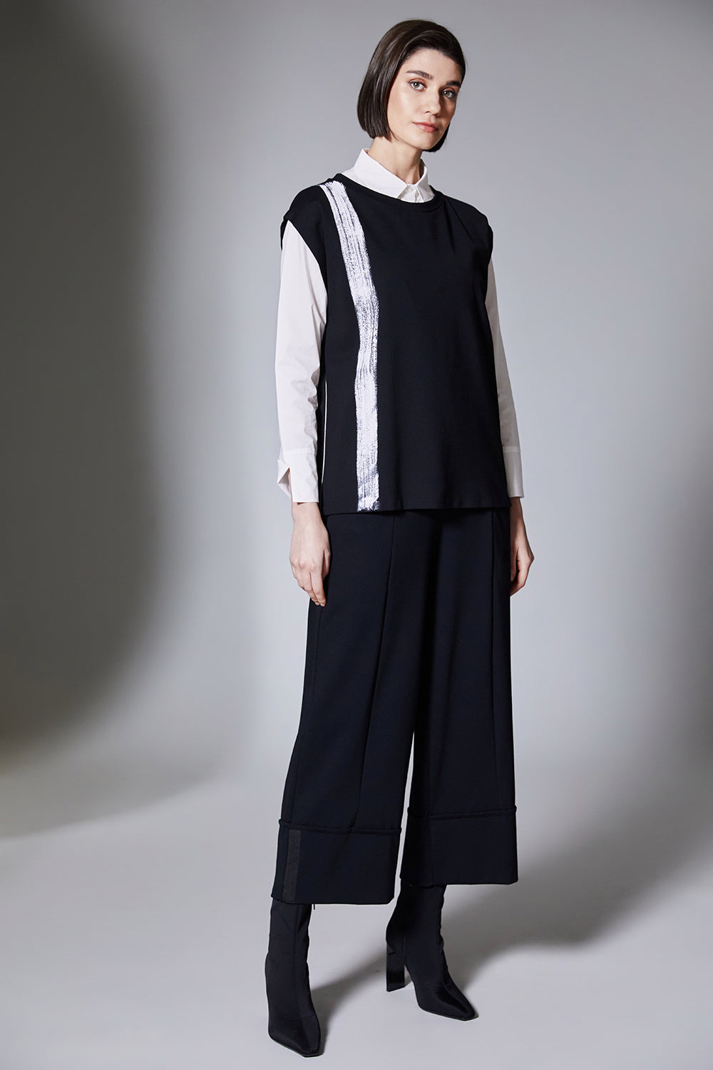 Woman wearing a black sleeveless top with white trim and wide-leg pants on a gray background