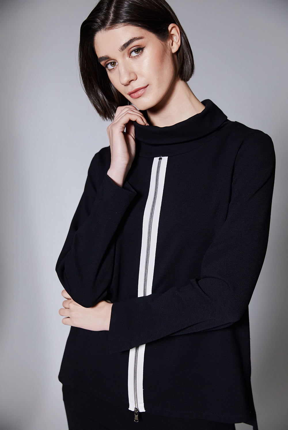 Woman wearing a black sweater with white stripe and front zip on a gray background