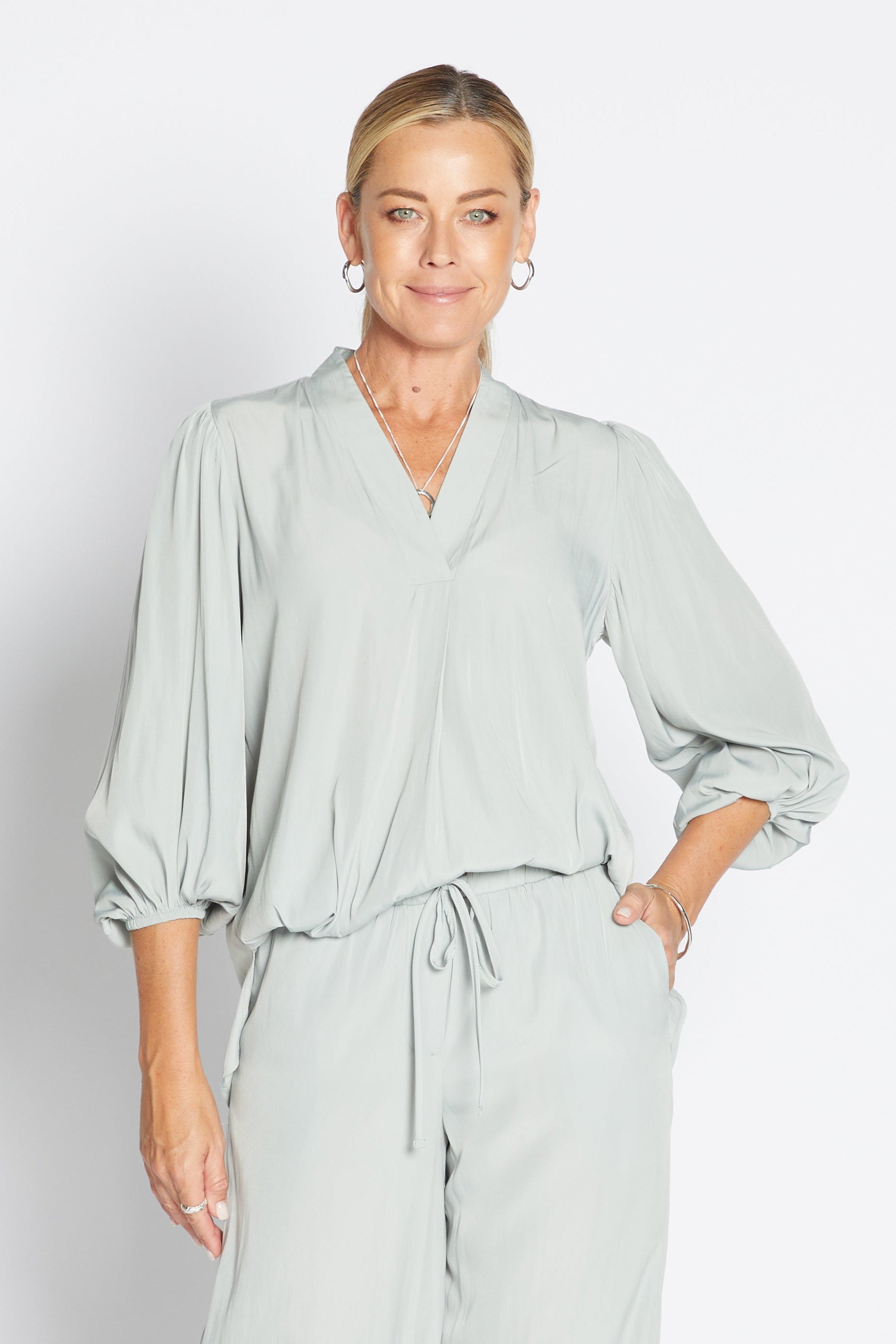 Woman wearing a sage green outfit against a plain background