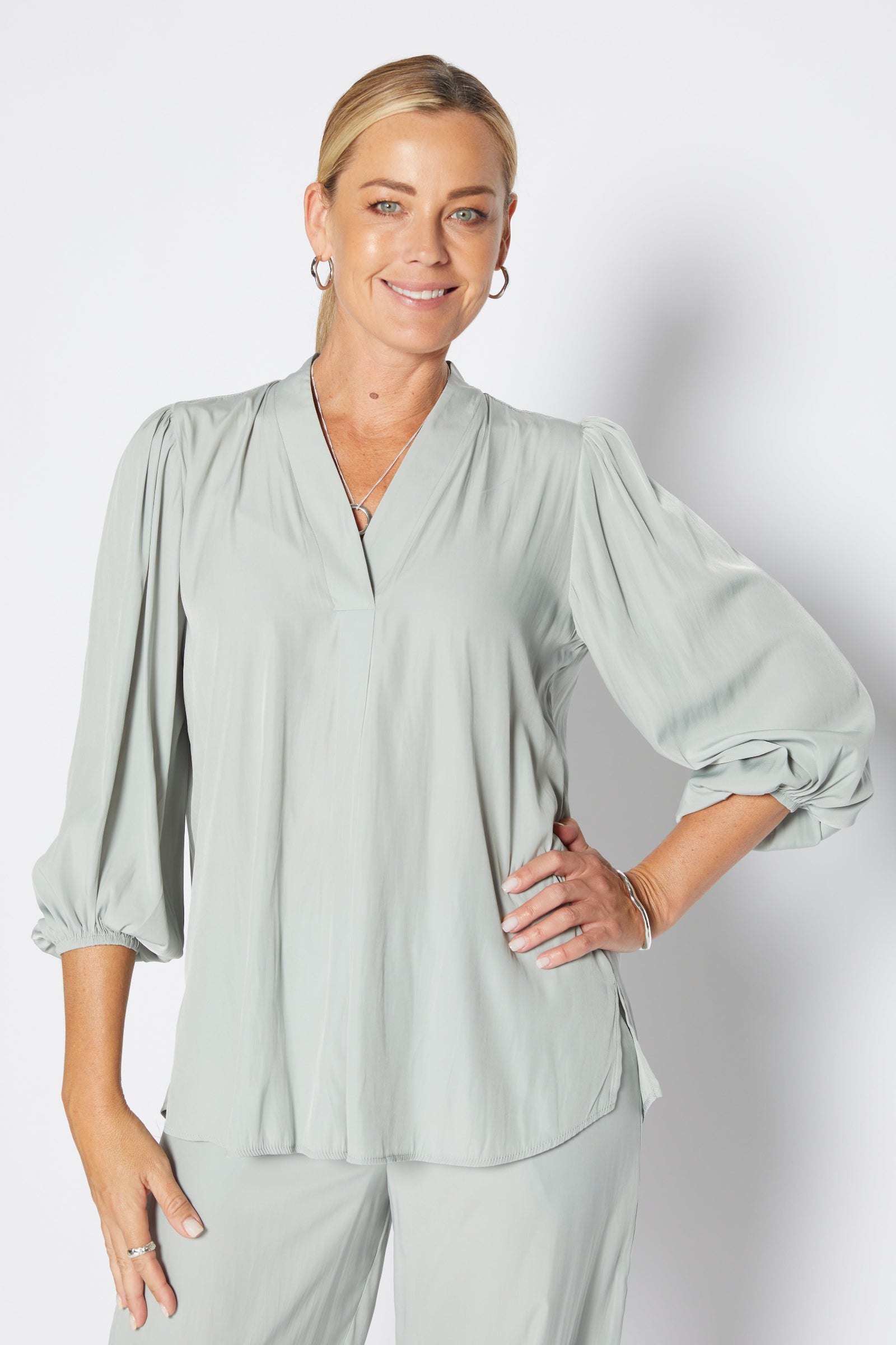Woman wearing a light green blouse and pants against a white background