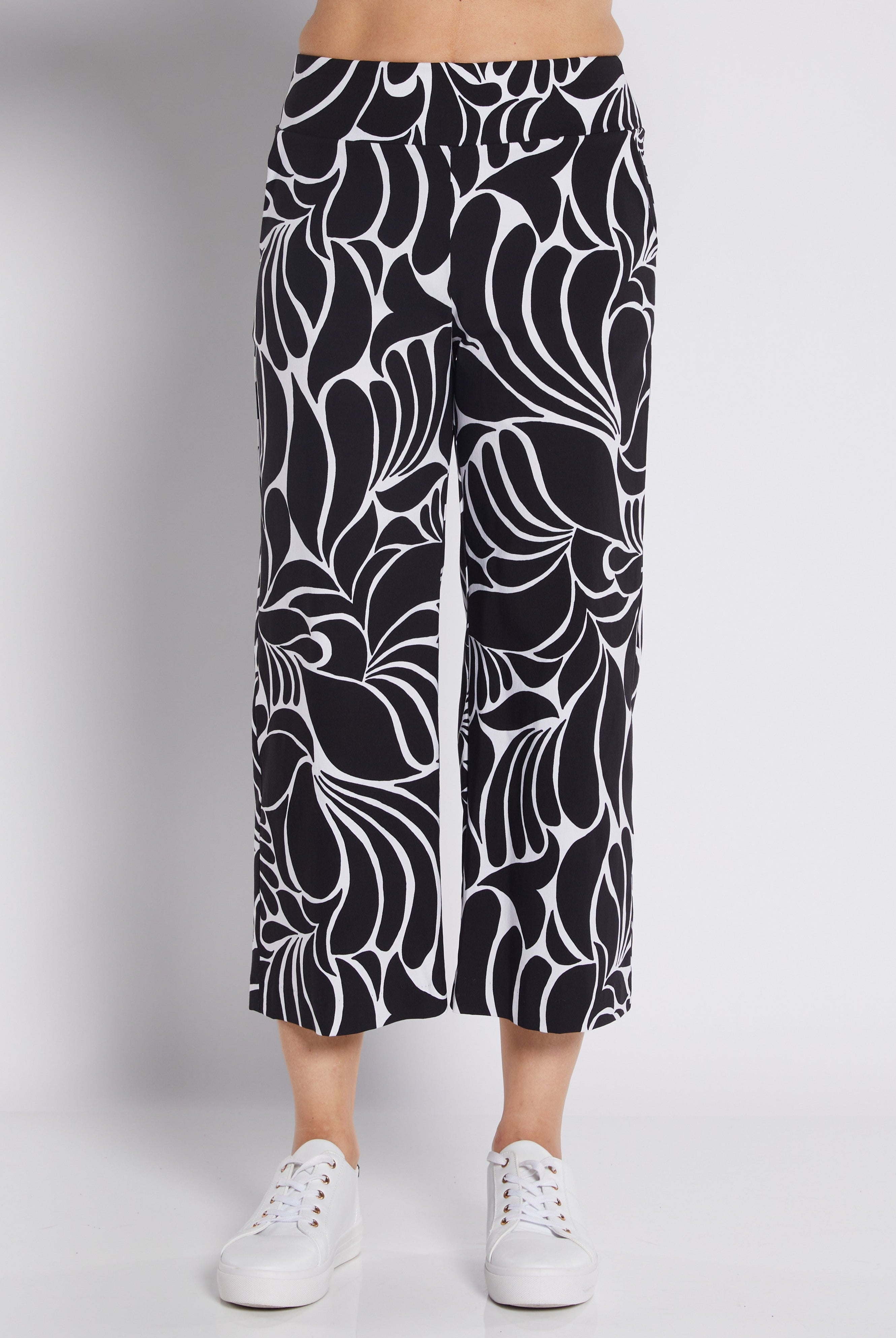 Black and white abstract floral print cropped pants worn by a model with white sneakers, photographed against a light gray studio background.