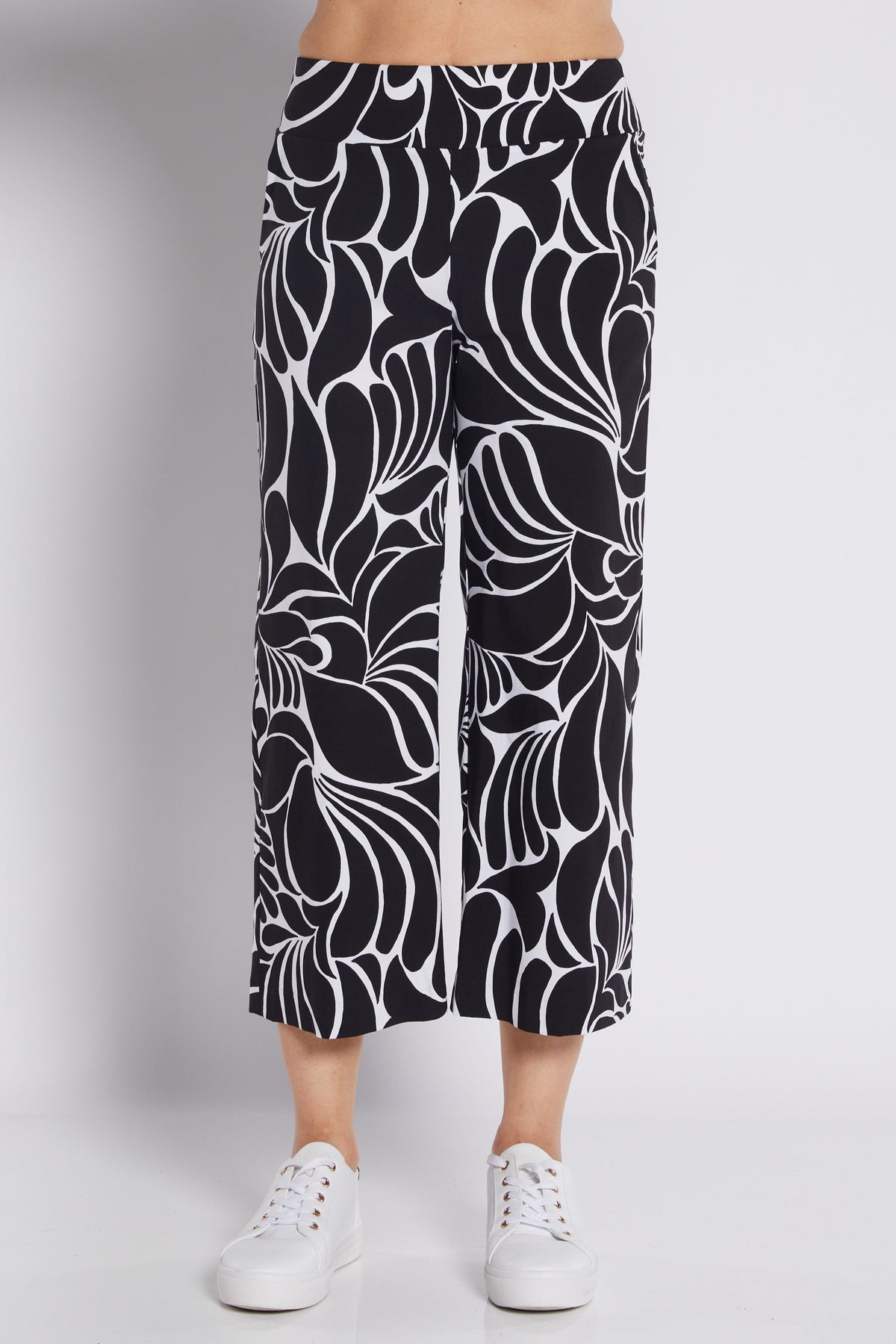 Black and white abstract floral print cropped pants worn by a model with white sneakers, photographed against a light gray studio background.
