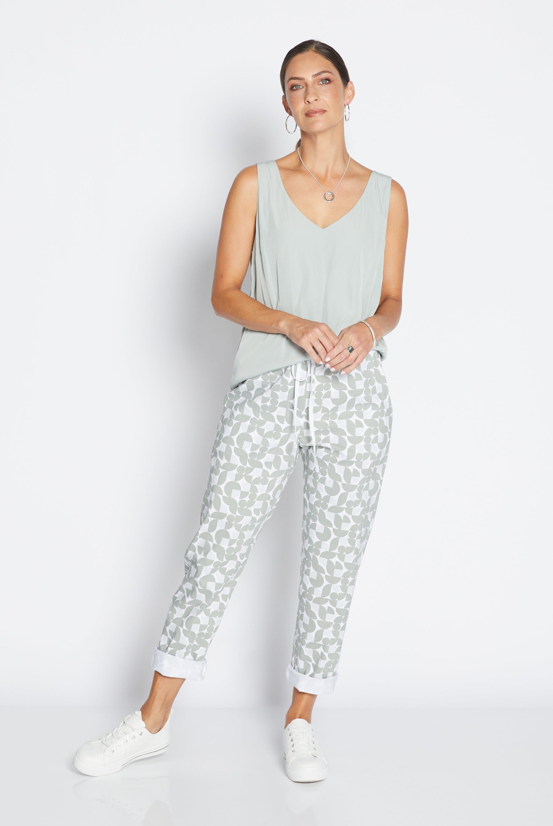 Woman wearing a light green sleeveless top and patterned pants on a white background