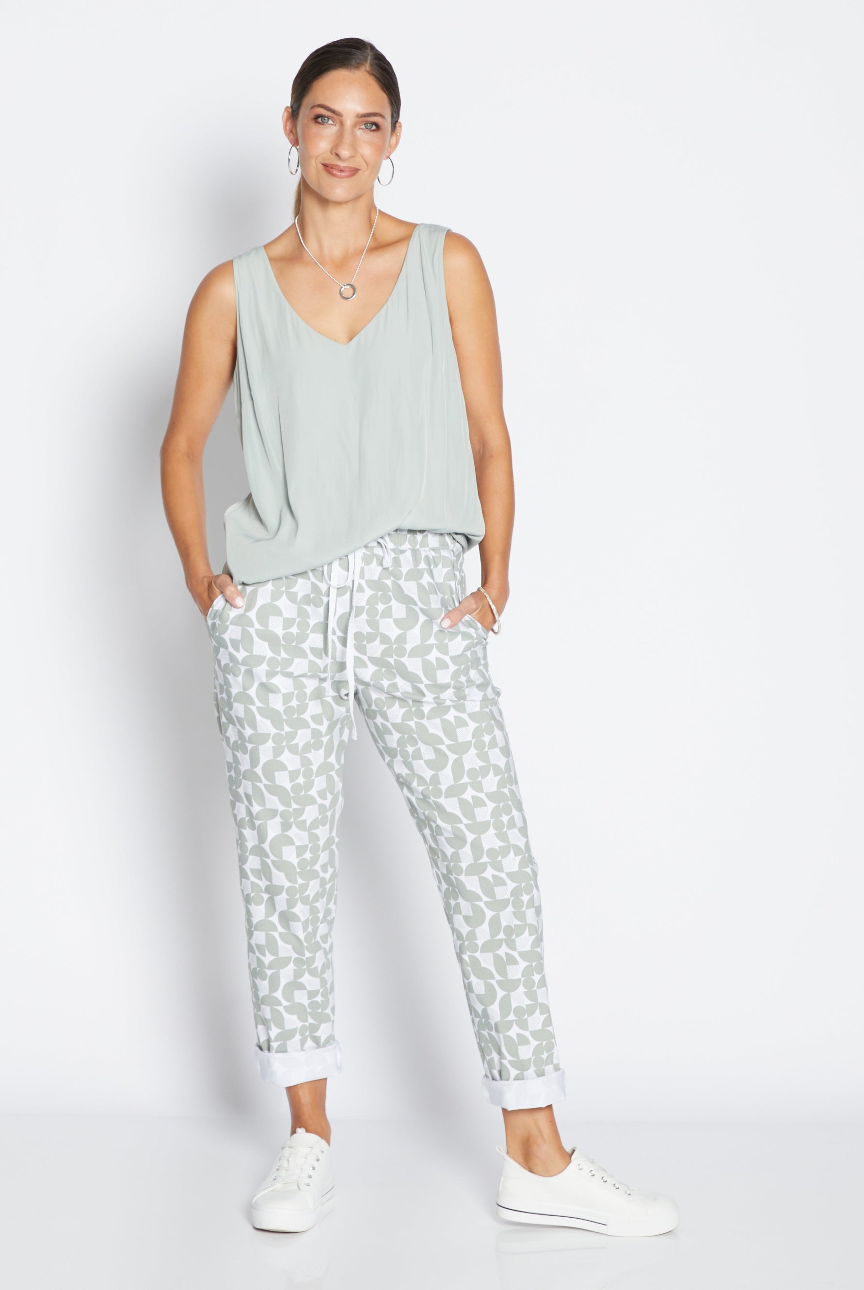 Woman wearing a light green sleeveless top and patterned pants on a white background