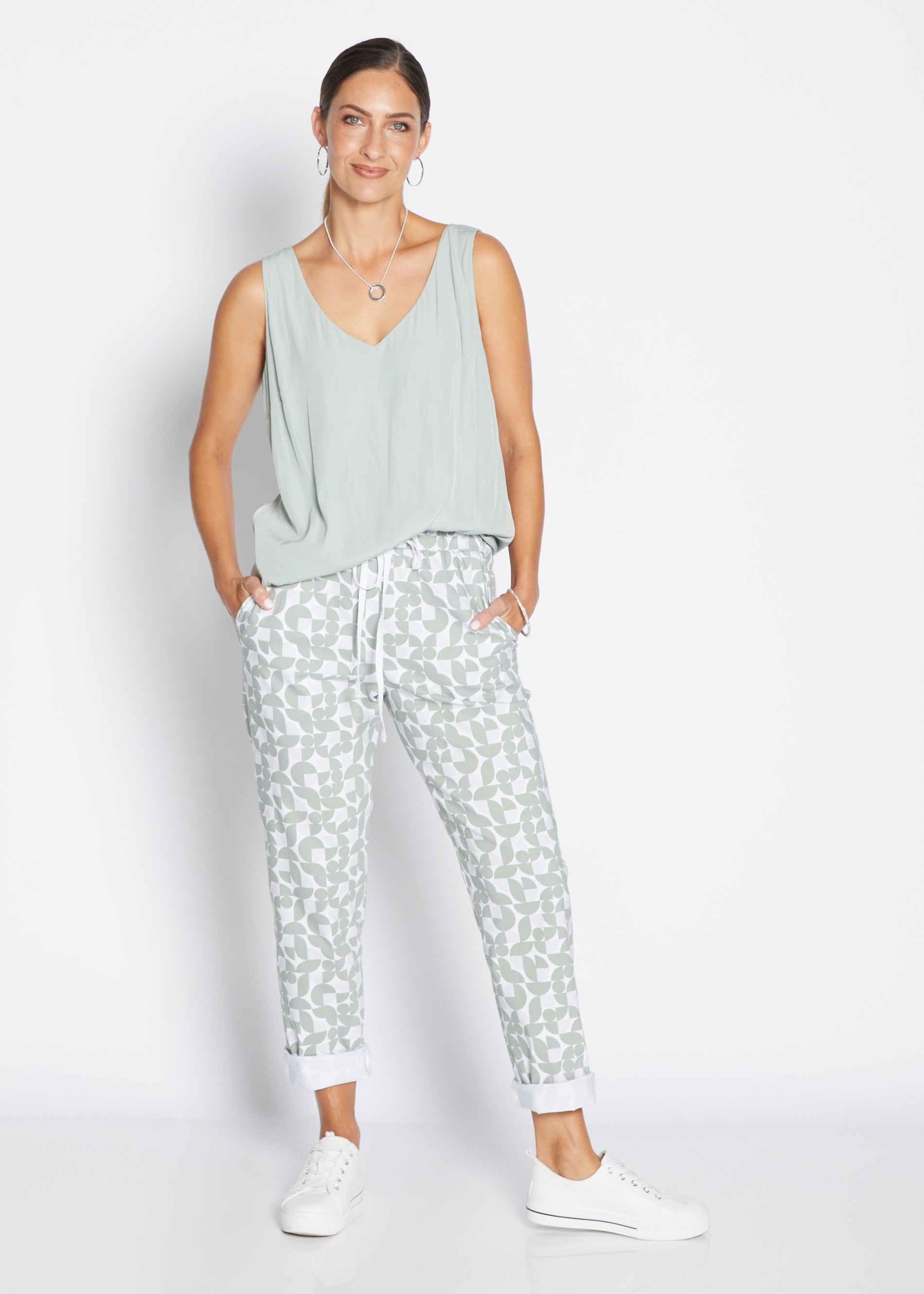 Woman wearing a light green sleeveless top and patterned pants on a white background