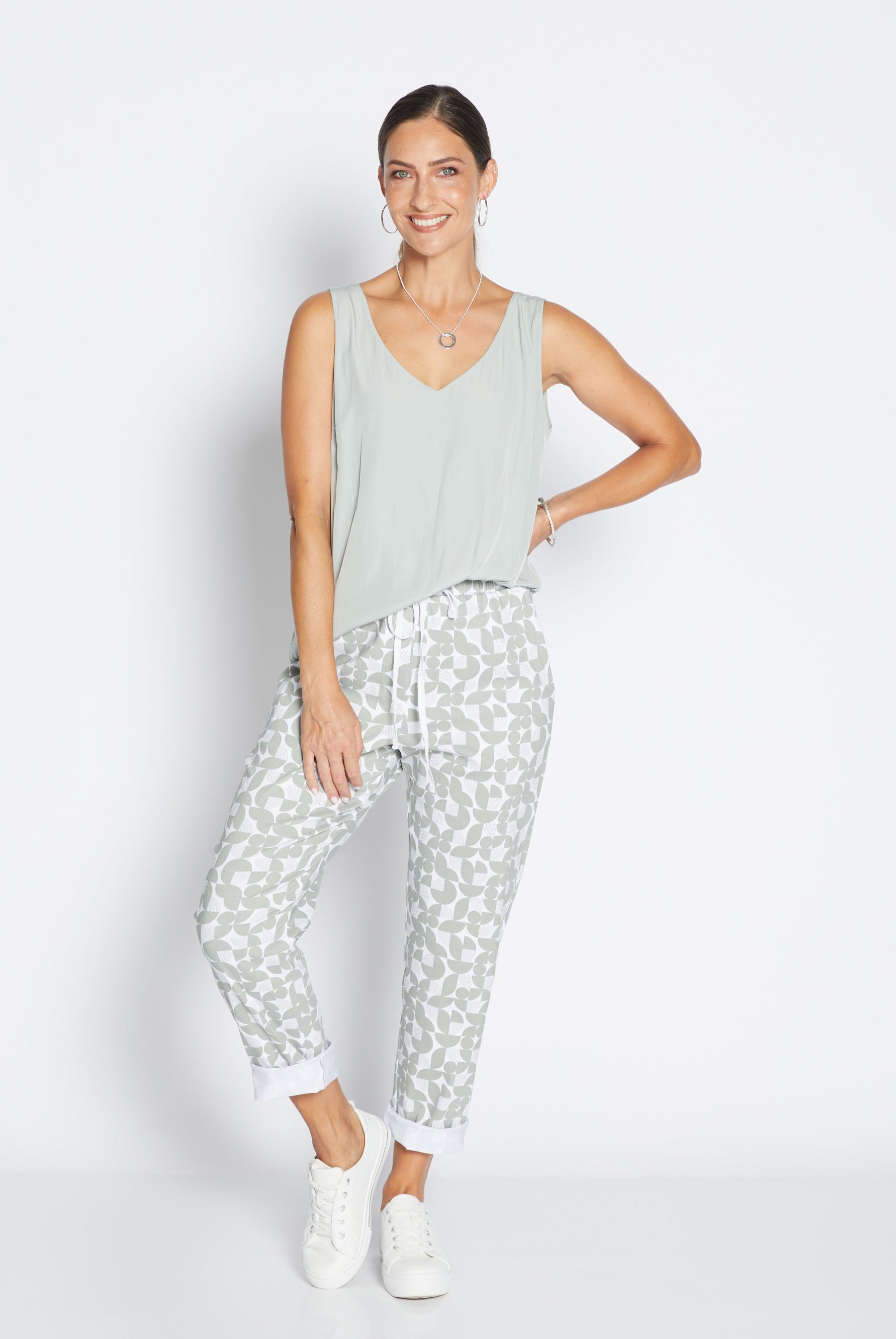 Woman wearing a light green sleeveless top and patterned pants on a white background
