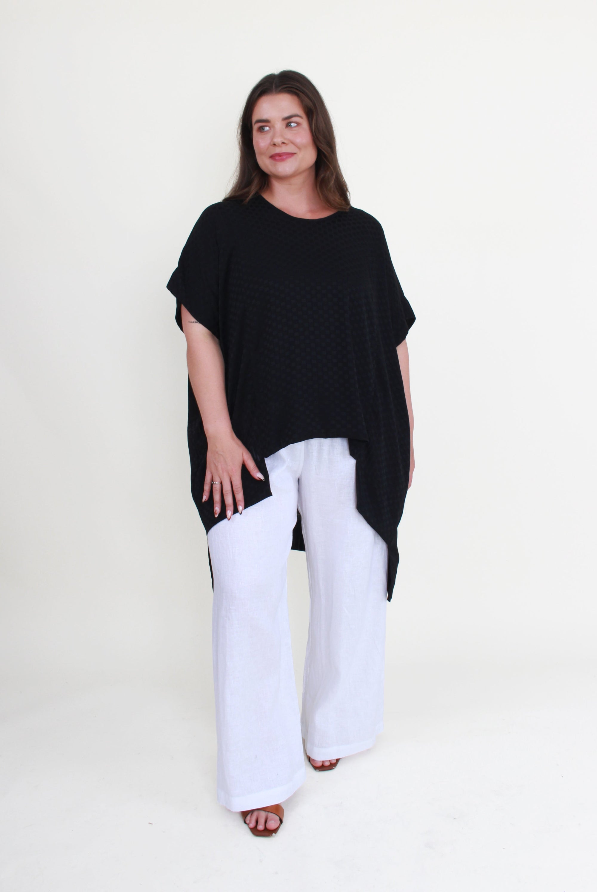 Woman wearing a black top and white pants on a white background