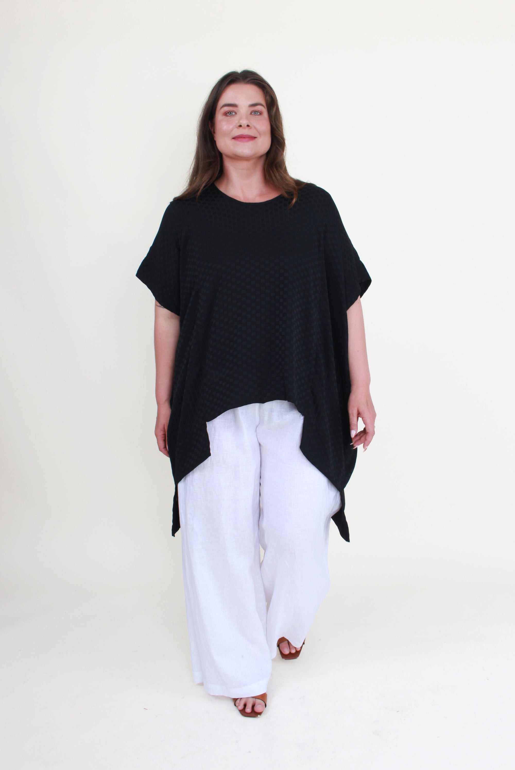 Woman wearing a black oversized top and white pants on a white background