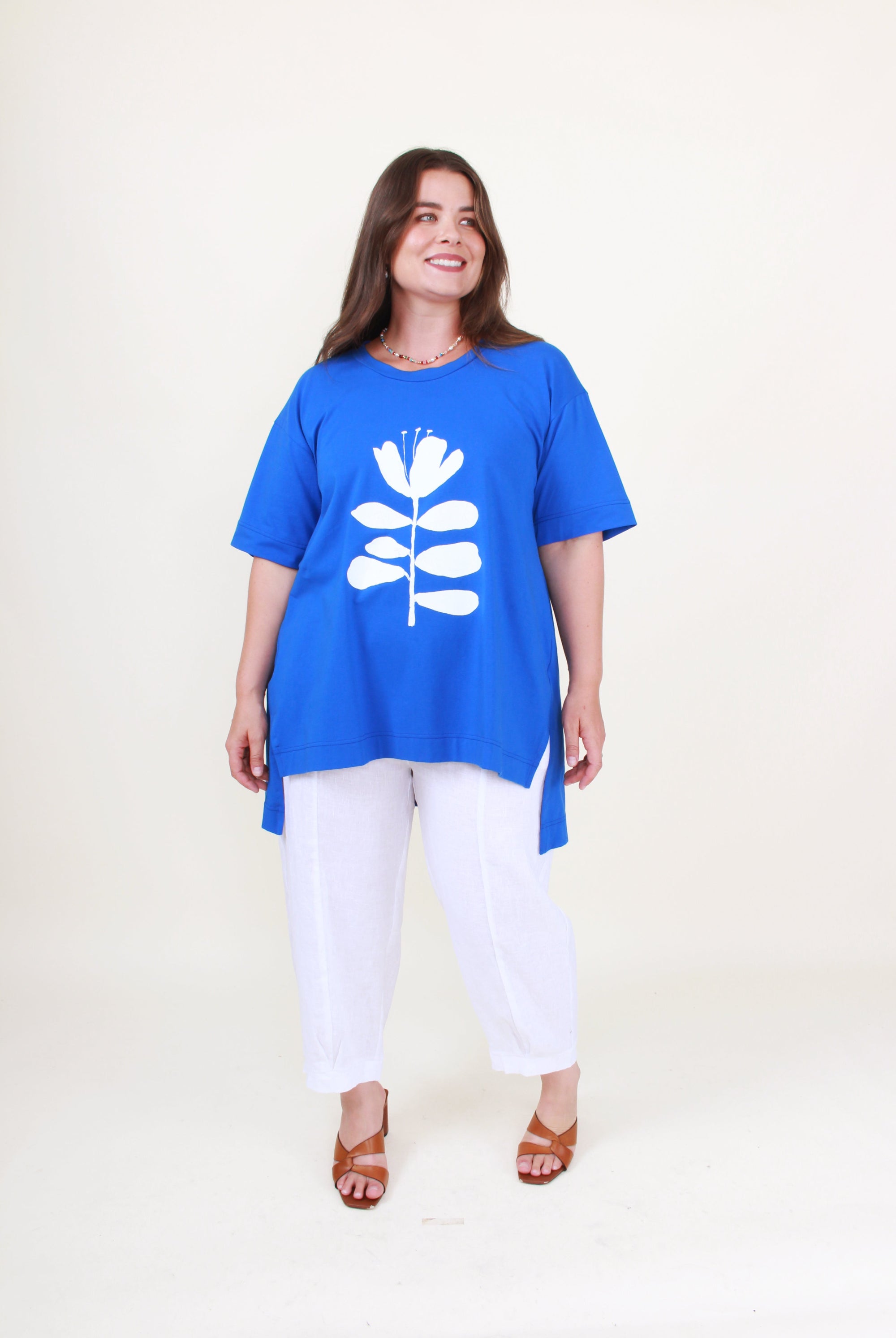 Woman wearing a blue tunic with a white floral design on a plain background