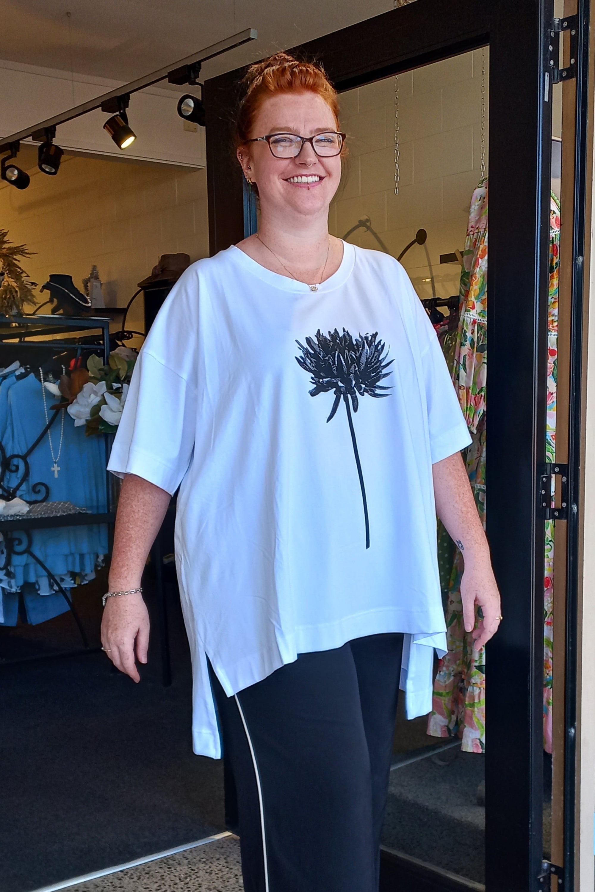 Woman wearing a white t-shirt with a black flower design, standing in a store.