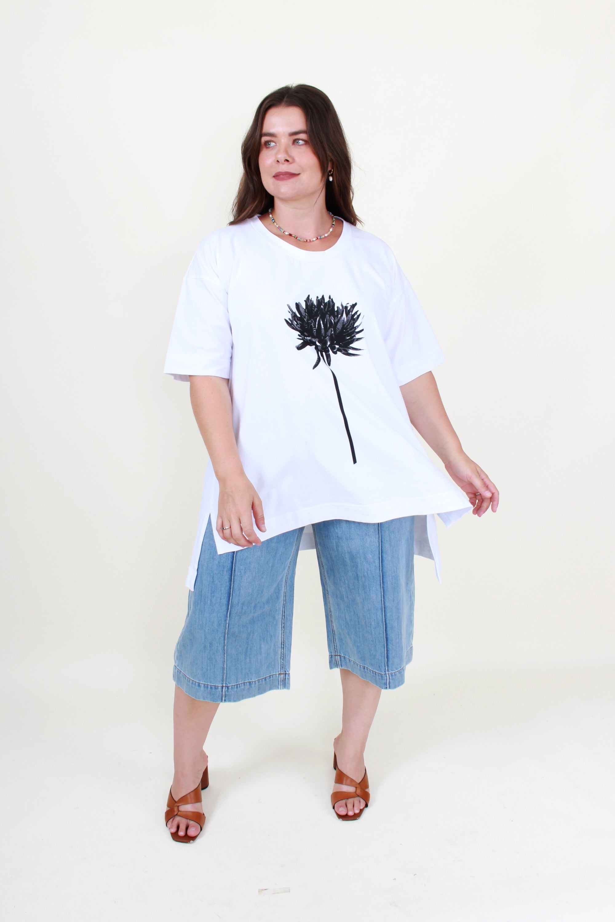 Woman wearing a white t-shirt with a black flower design and blue jeans on a white background