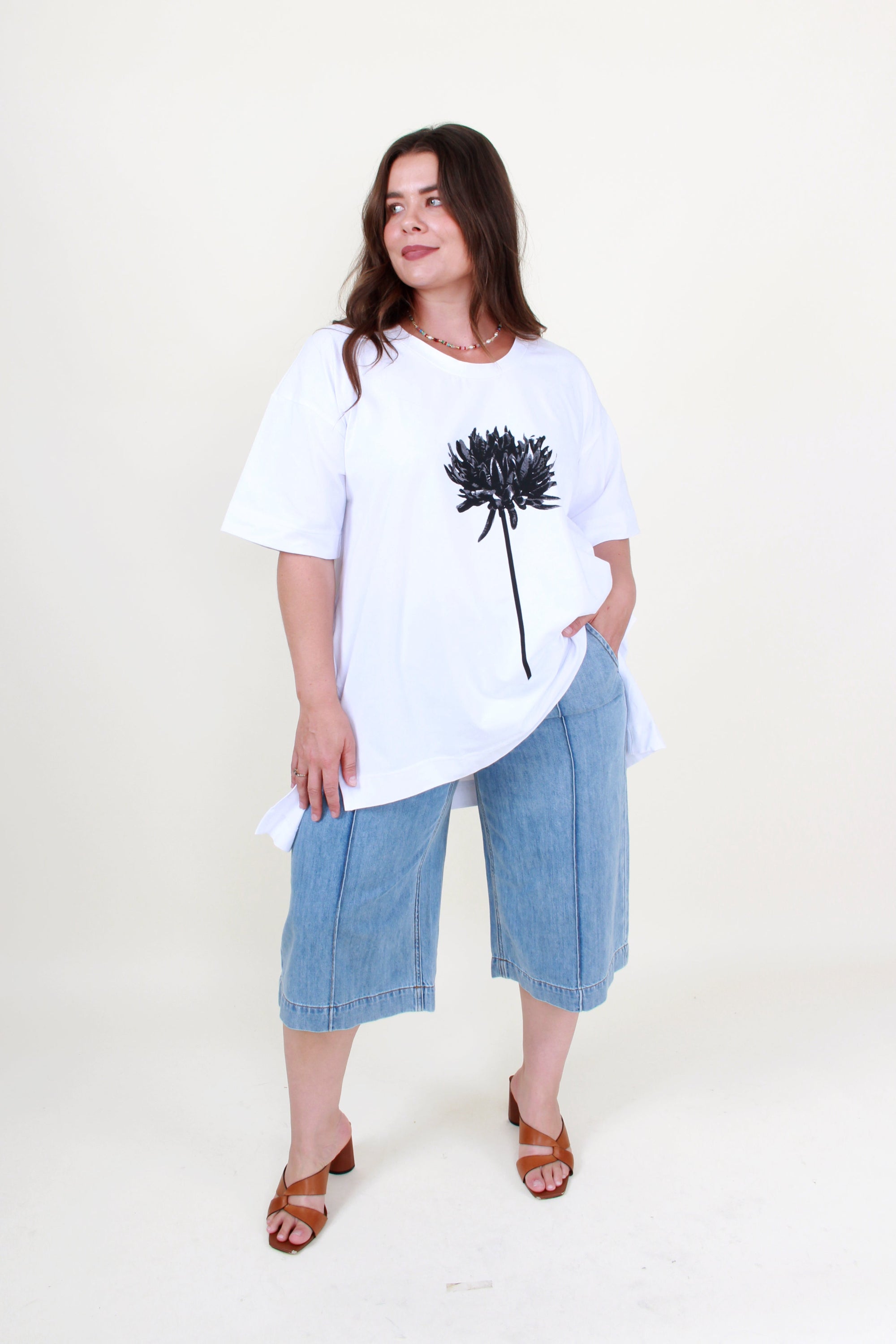Woman wearing a white t-shirt with a black flower design and blue jeans on a white background