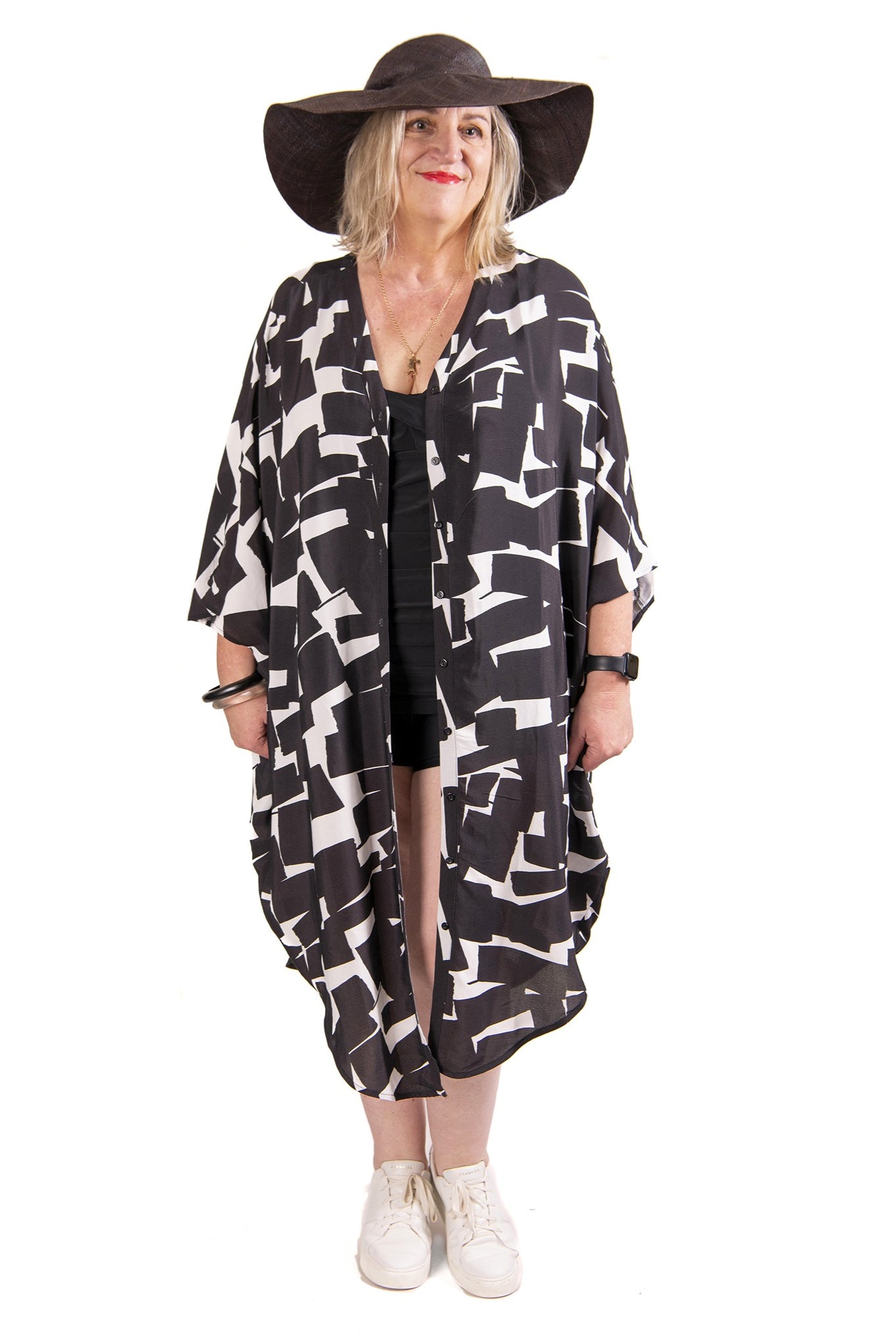 Woman wearing a black and white patterned kaftan and wide-brimmed hat on a white background.