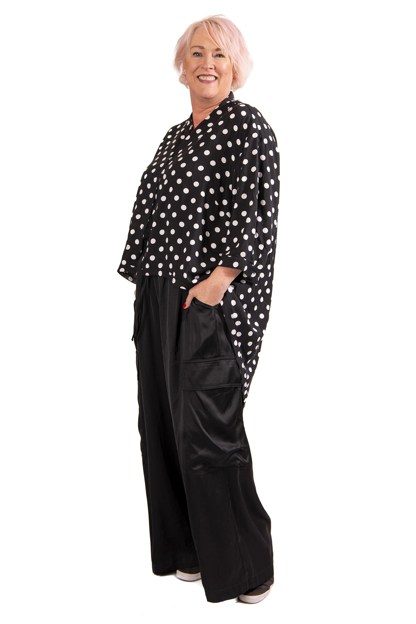 Woman wearing a black polka dot blouse and black wide-leg pants on a white background