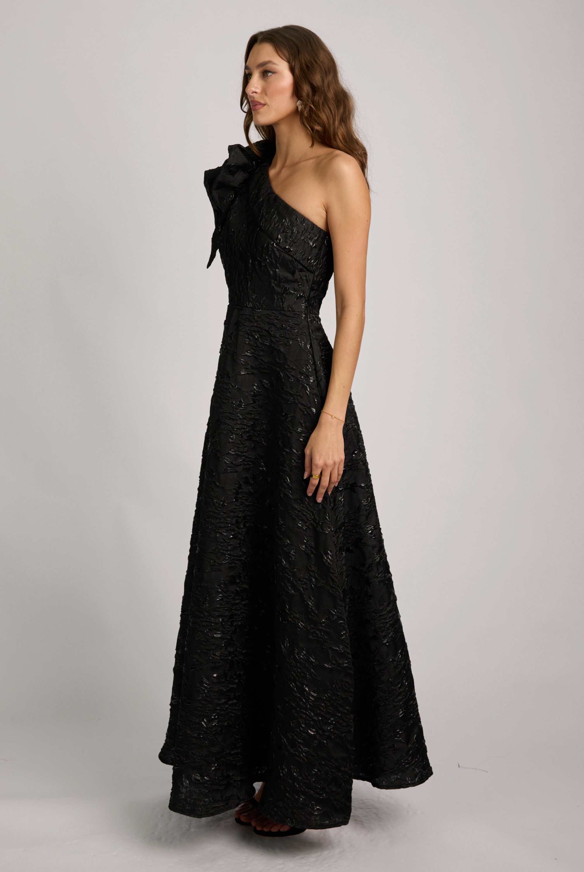 Woman wearing a black one-shoulder dress with a bow detail on a gray background